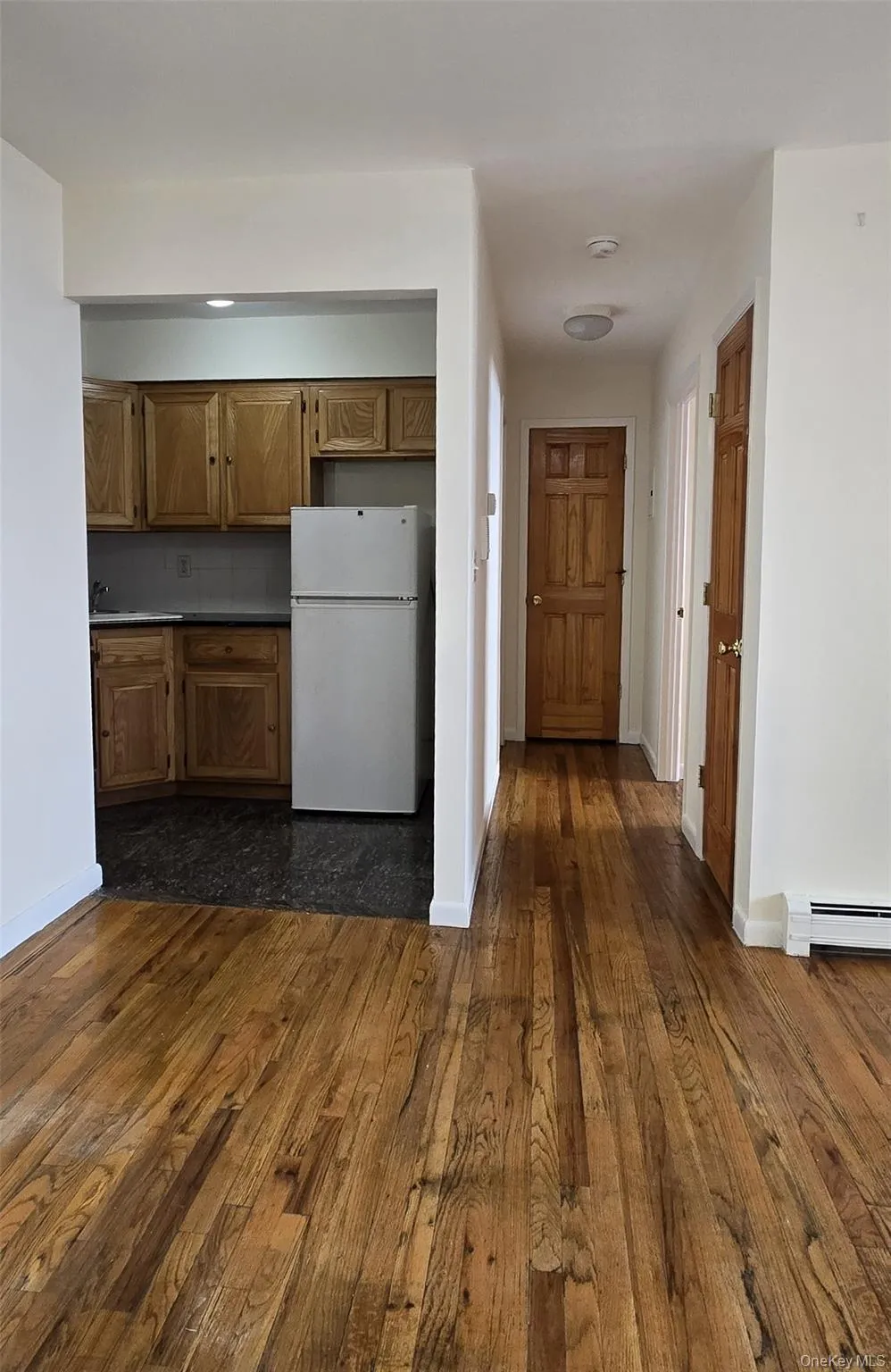 Kitchen with brown cabinets, freestanding refrigerator, a baseboard radiator, and dark wood-style floors Kitchen with brown cabinets, freestanding refrigerator, a baseboard radiator, and dark wood-style floors