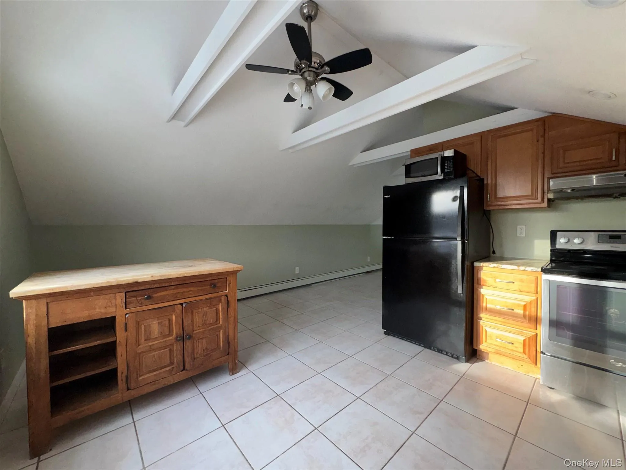 Kitchen with appliances with stainless steel finishes, brown cabinetry, light countertops, under cabinet range hood, and baseboard heating Kitchen with appliances with stainless steel finishes, brown cabinetry, light countertops, under cabinet range hood, and baseboard heating