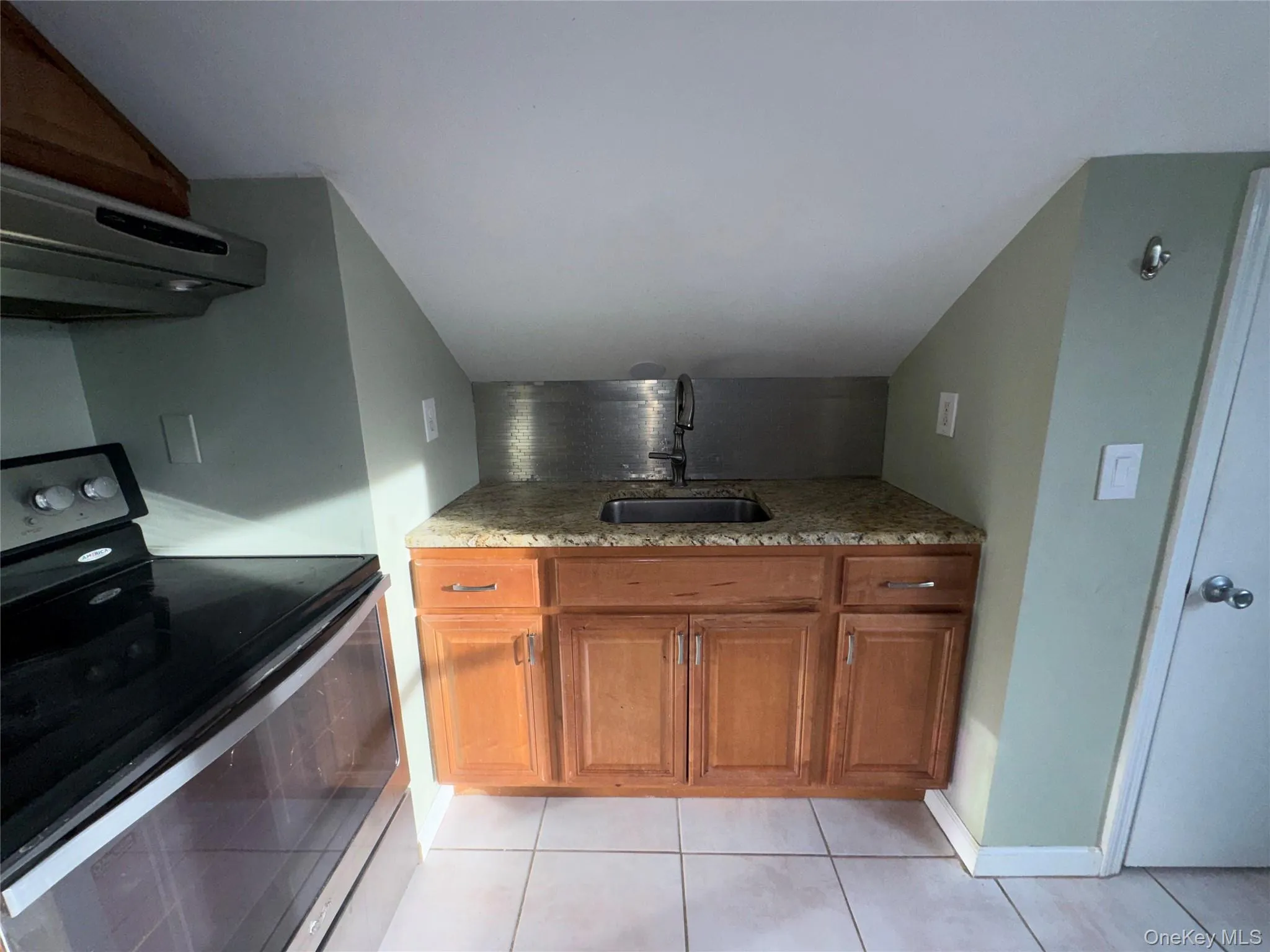 Kitchen with stainless steel electric range, brown cabinetry, extractor fan, and light stone counters Kitchen with stainless steel electric range, brown cabinetry, extractor fan, and light stone counters