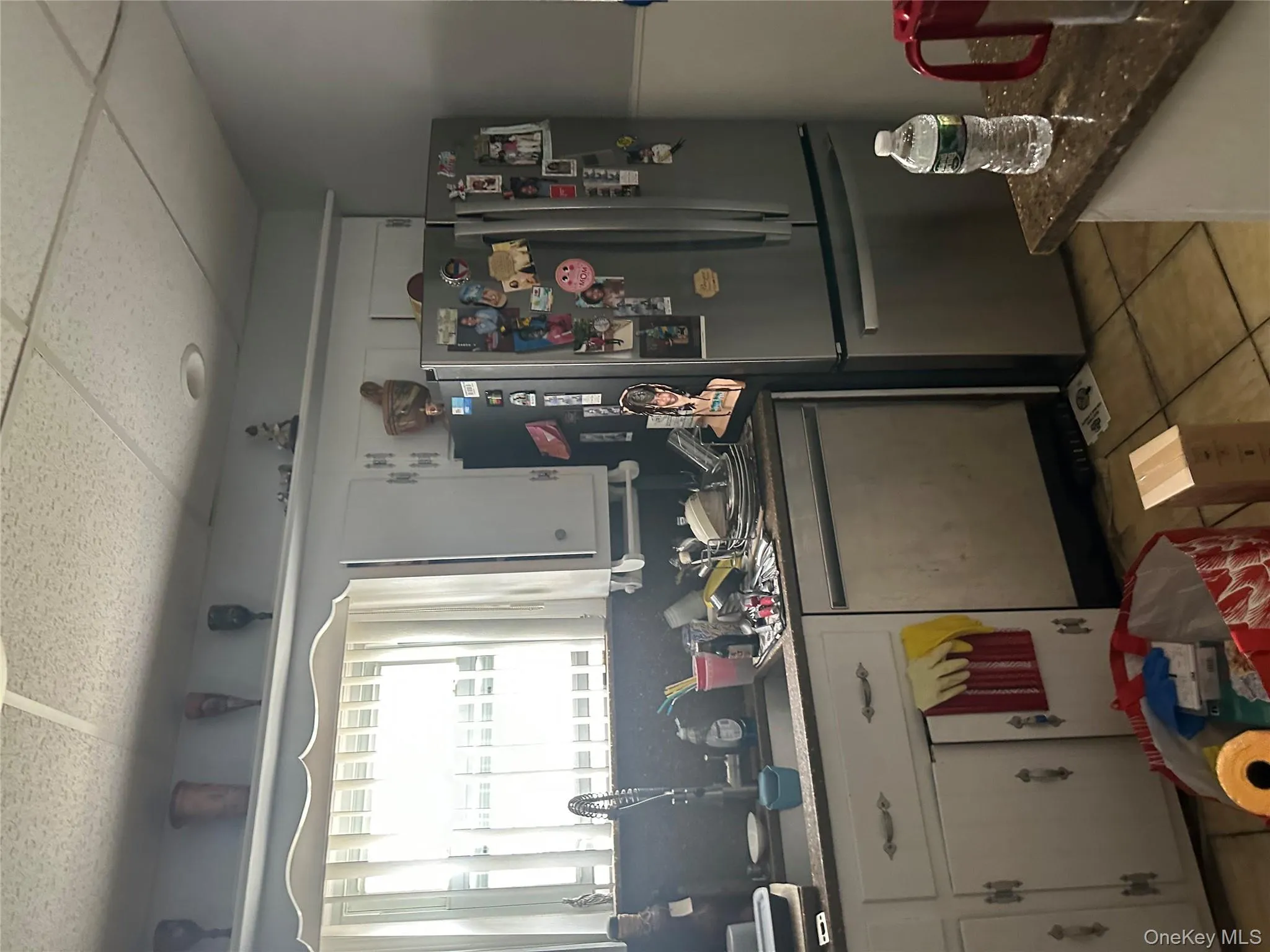 Kitchen with white cabinetry, fridge, light tile patterned flooring, dishwashing machine, and a drop ceiling Kitchen with white cabinetry, fridge, light tile patterned flooring, dishwashing machine, and a drop ceiling
