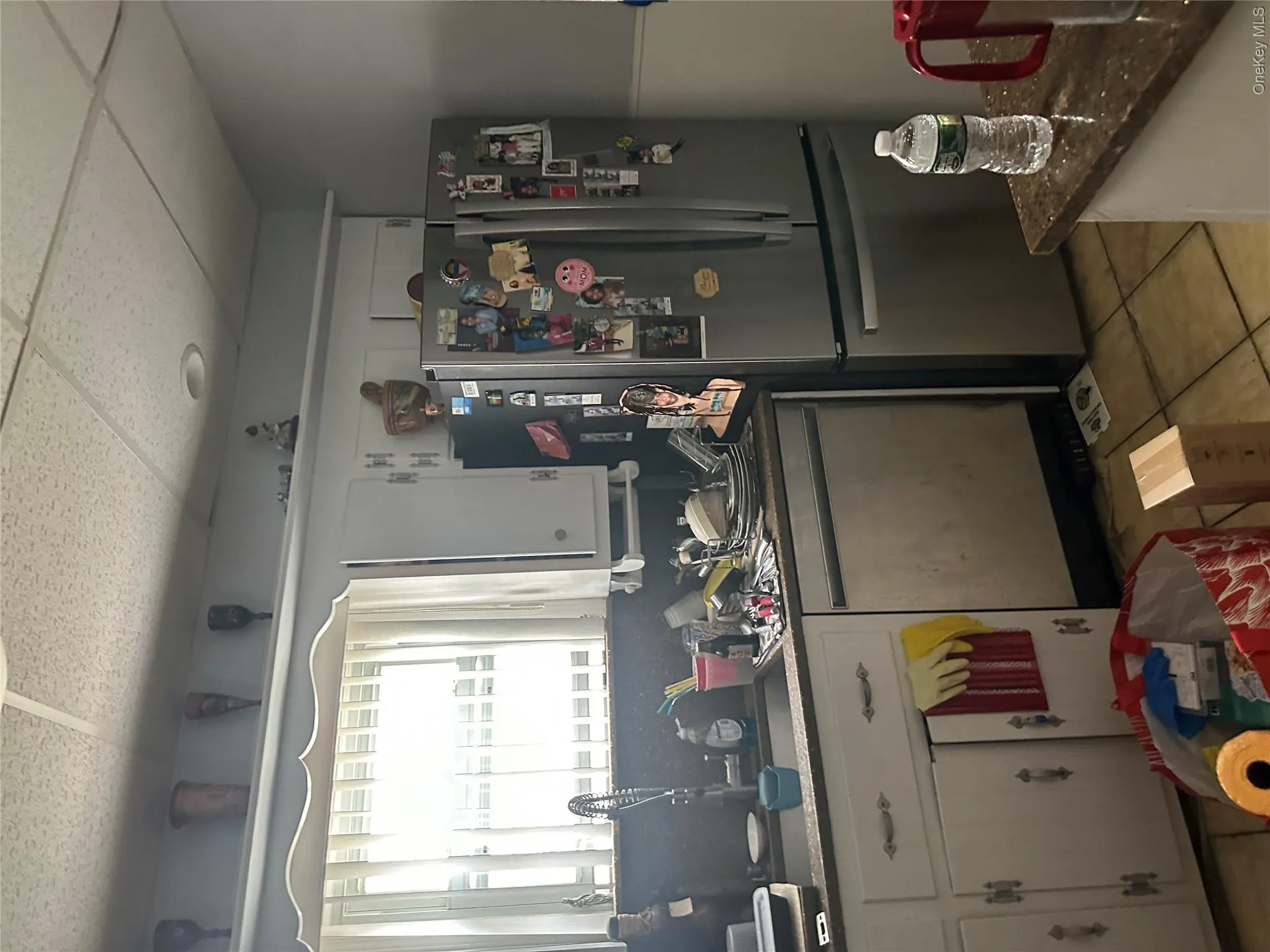 Kitchen with white cabinetry, fridge, light tile patterned flooring, dishwashing machine, and a drop ceiling Kitchen with white cabinetry, fridge, light tile patterned flooring, dishwashing machine, and a drop ceiling