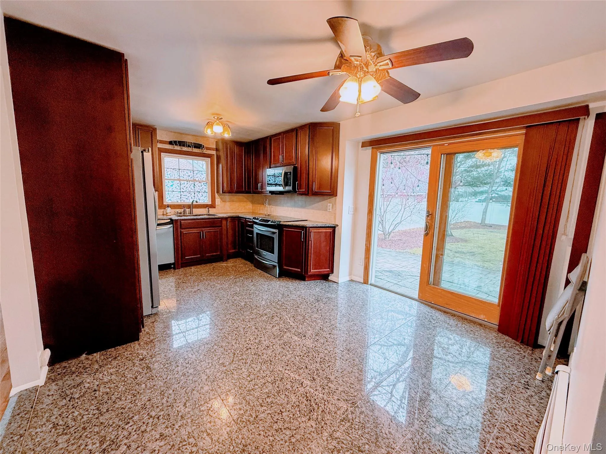 Kitchen with granite floors, appliances with stainless steel finishes, light countertops, ceiling fan, and backsplash Kitchen with granite floors, appliances with stainless steel finishes, light countertops, ceiling fan, and backsplash