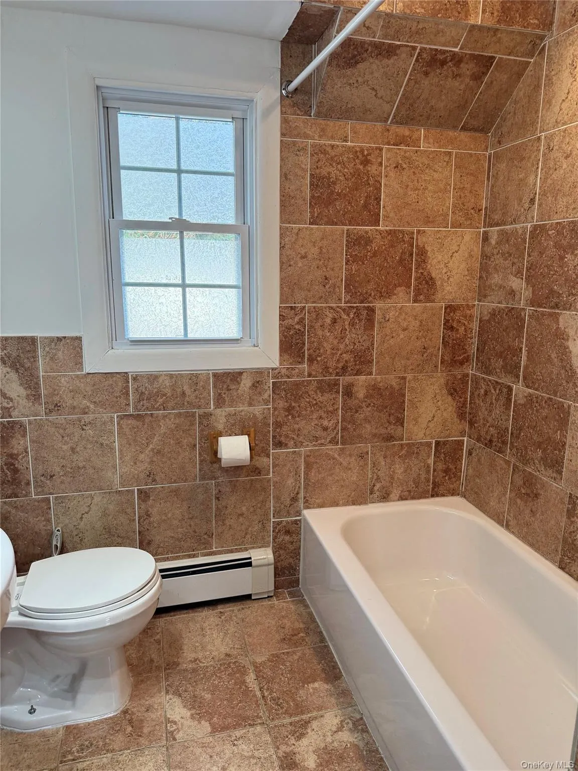 Full bath featuring tile walls, shower / tub combination, and a baseboard heat Full bath featuring tile walls, shower / tub combination, and a baseboard heat