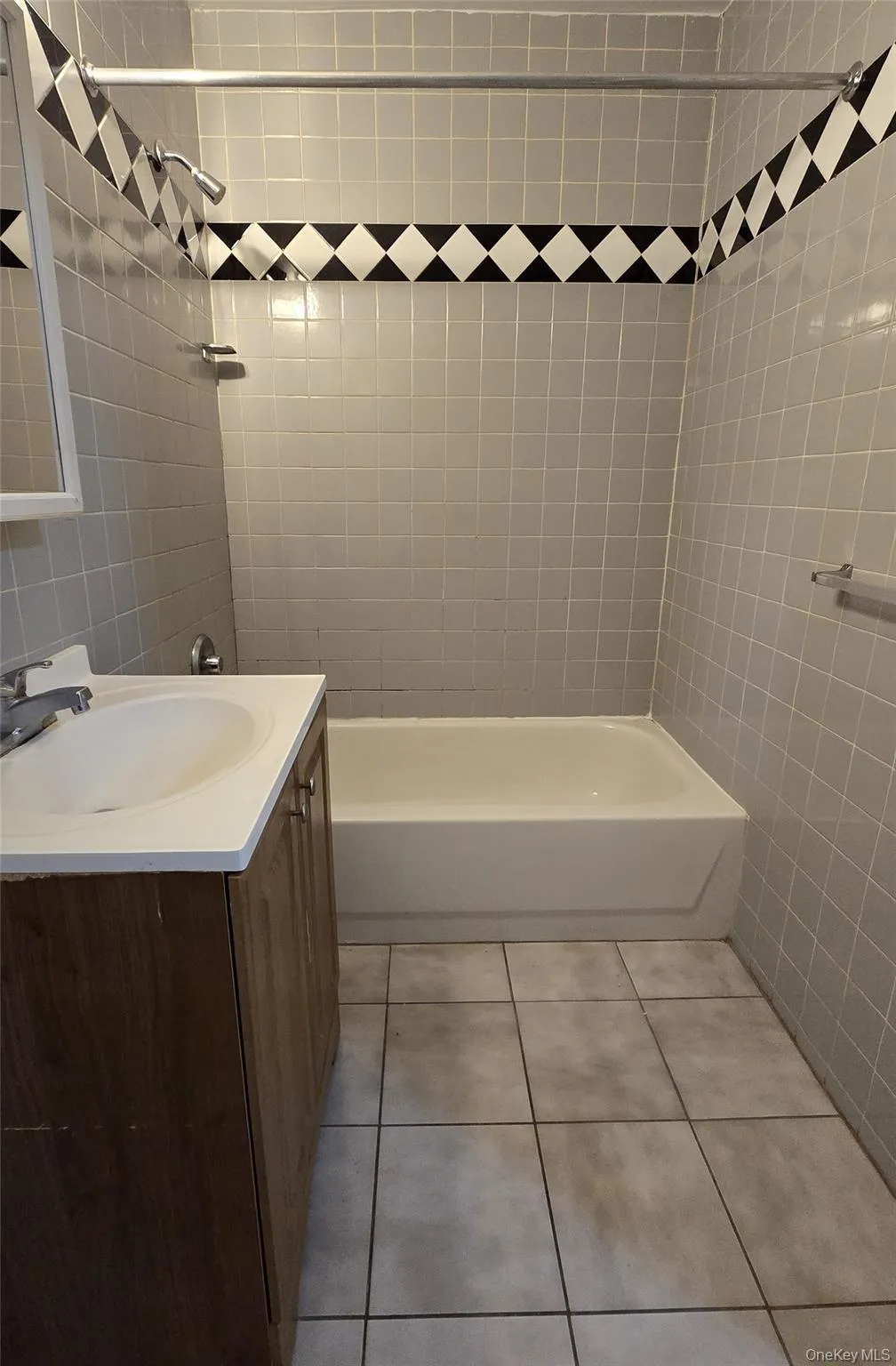Bathroom with light tile patterned floors, shower / washtub combination, vanity, and tile walls Bathroom with light tile patterned floors, shower / washtub combination, vanity, and tile walls