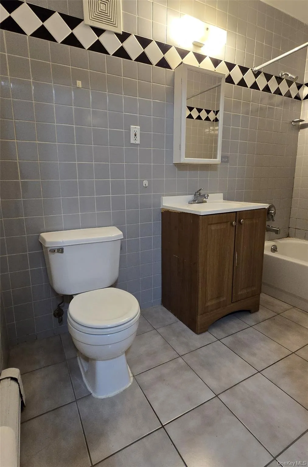 Full bathroom featuring tile walls, vanity, light tile patterned floors, tub / shower combination, and a baseboard heating unit Full bathroom featuring tile walls, vanity, light tile patterned floors, tub / shower combination, and a baseboard heating unit
