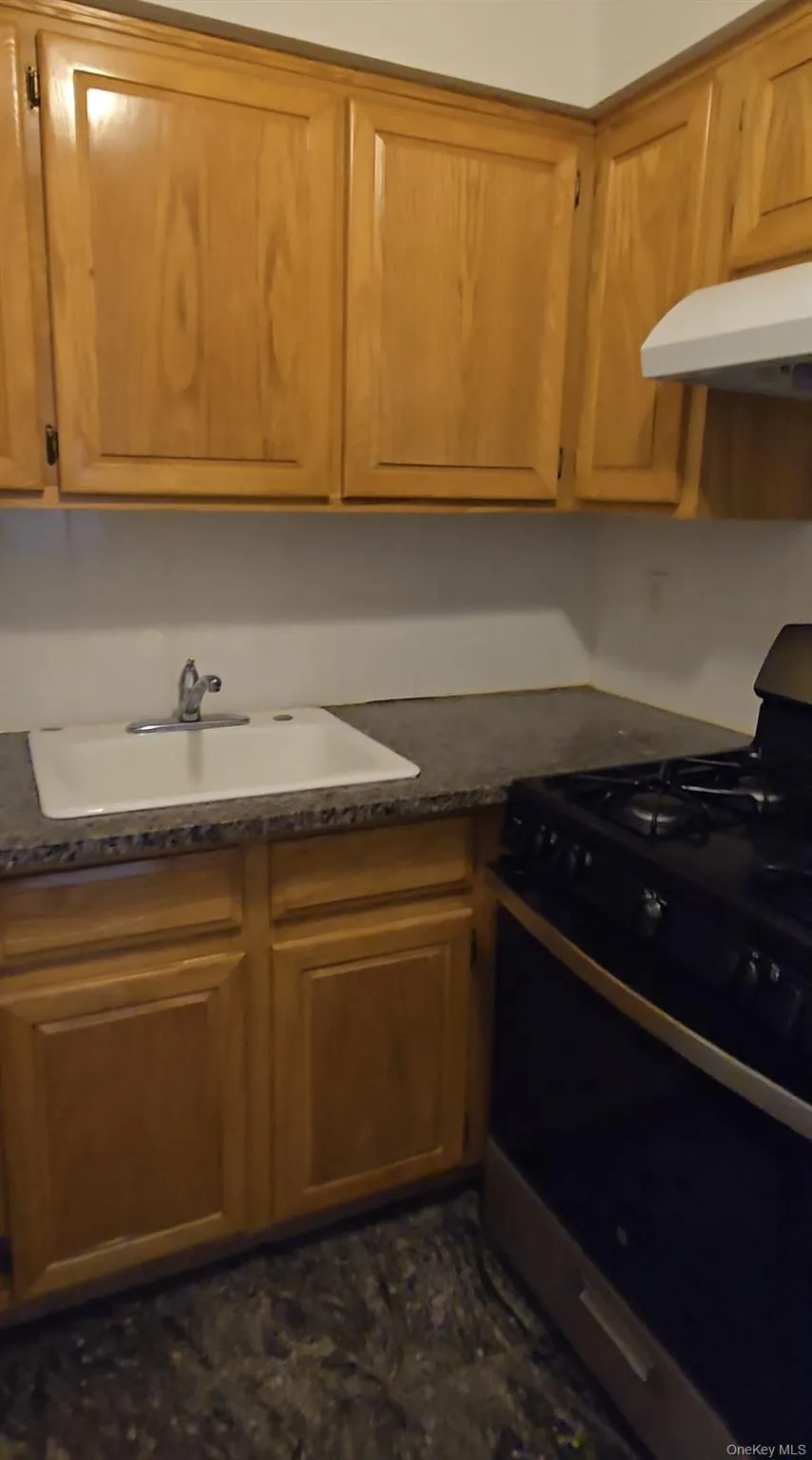 Kitchen with range with gas stovetop, under cabinet range hood, and brown cabinetry Kitchen with range with gas stovetop, under cabinet range hood, and brown cabinetry