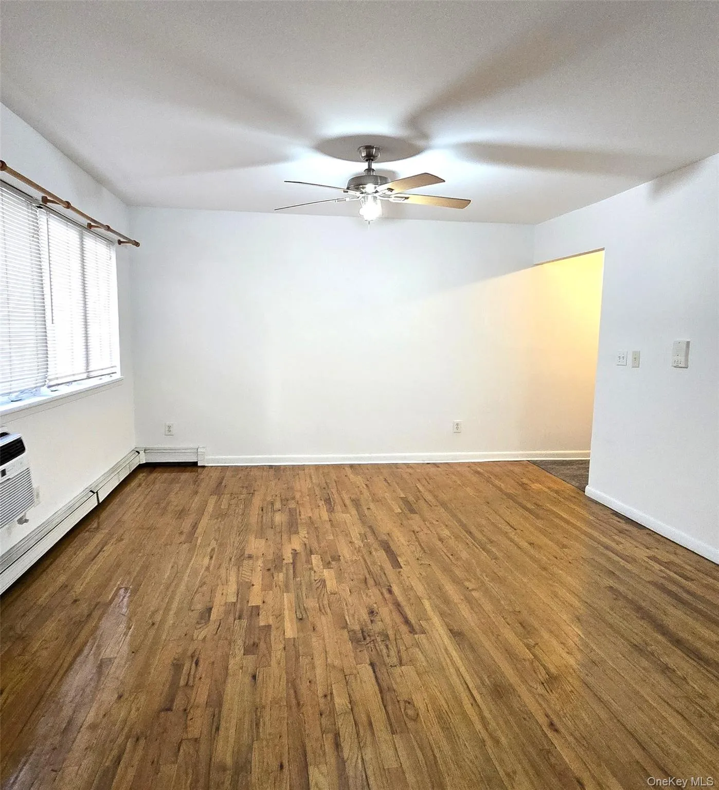 Empty room with baseboard heating, dark wood-type flooring, and a ceiling fan Empty room with baseboard heating, dark wood-type flooring, and a ceiling fan