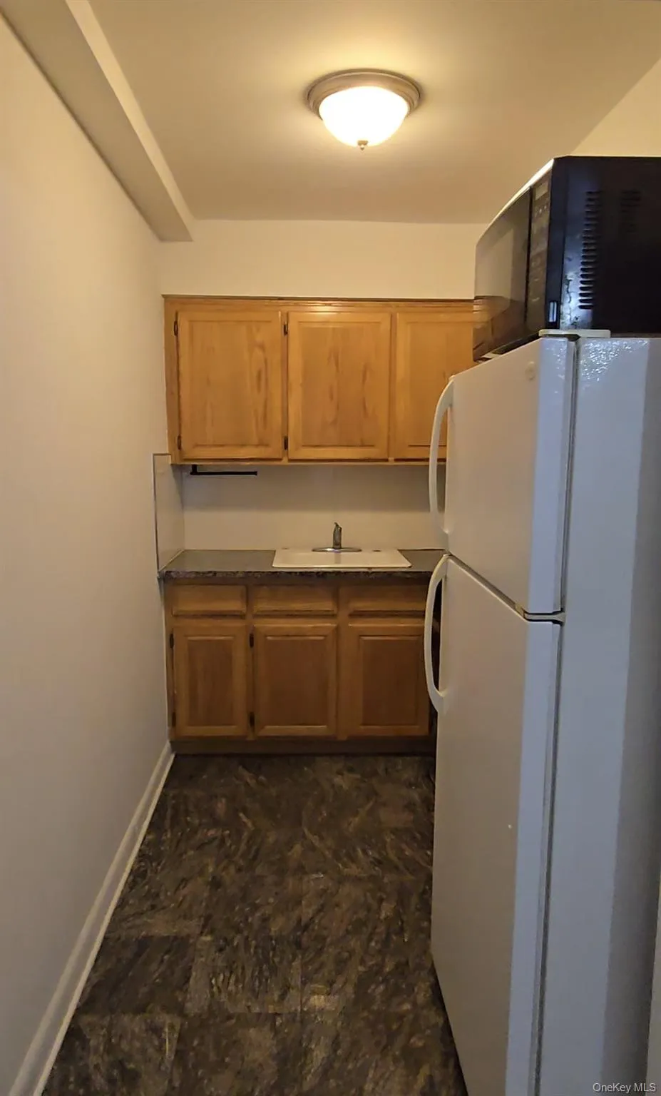 Kitchen featuring freestanding refrigerator, black microwave, and dark countertops Kitchen featuring freestanding refrigerator, black microwave, and dark countertops