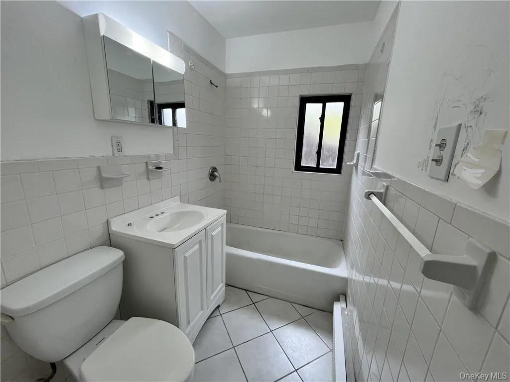 Full bath featuring tile walls, vanity, tub / shower combination, wainscoting, and light tile patterned floors Full bath featuring tile walls, vanity, tub / shower combination, wainscoting, and light tile patterned floors