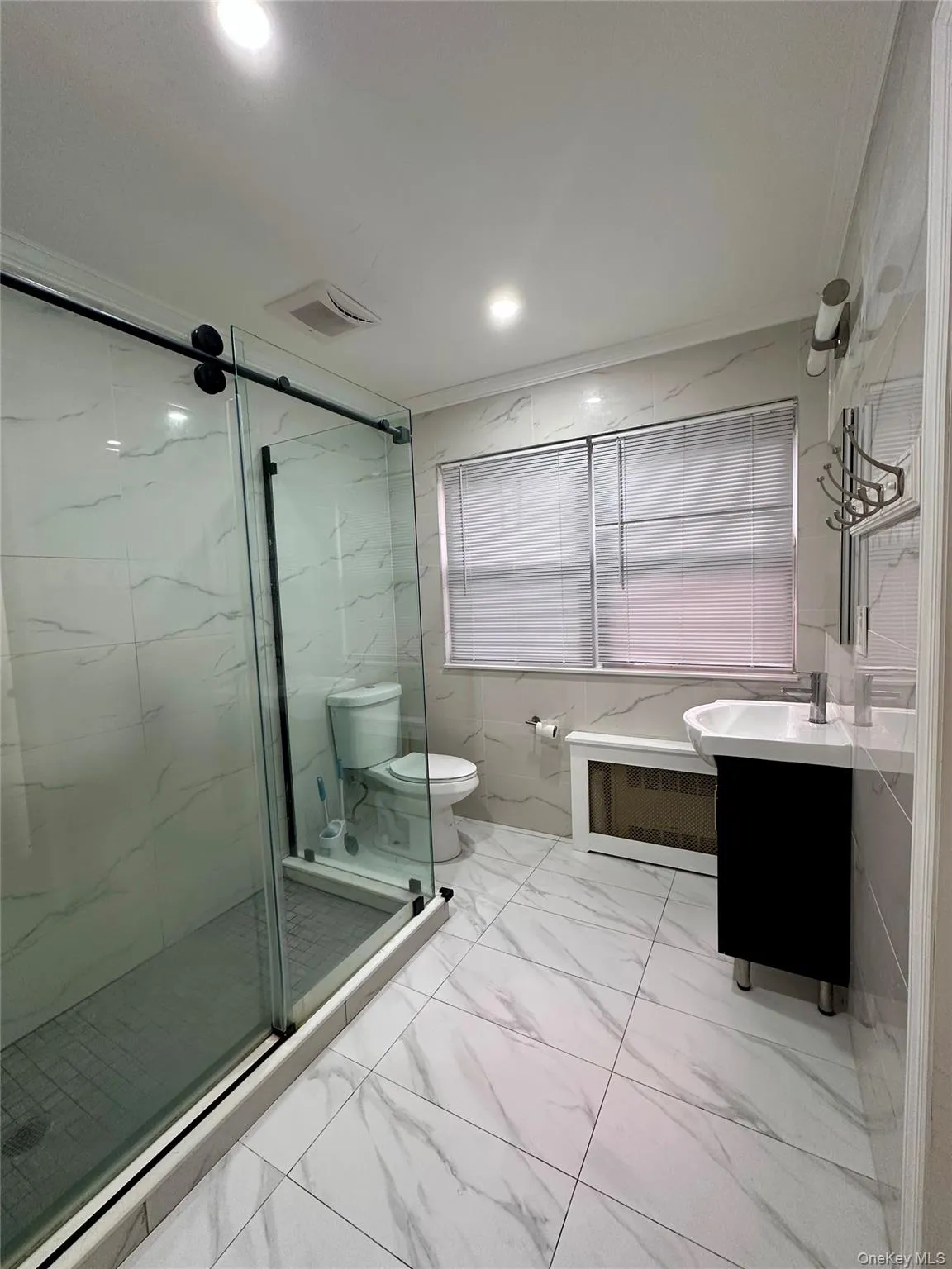 Bathroom featuring vanity, light marble finish flooring, a marble finish shower, recessed lighting, and tile walls Bathroom featuring vanity, light marble finish flooring, a marble finish shower, recessed lighting, and tile walls