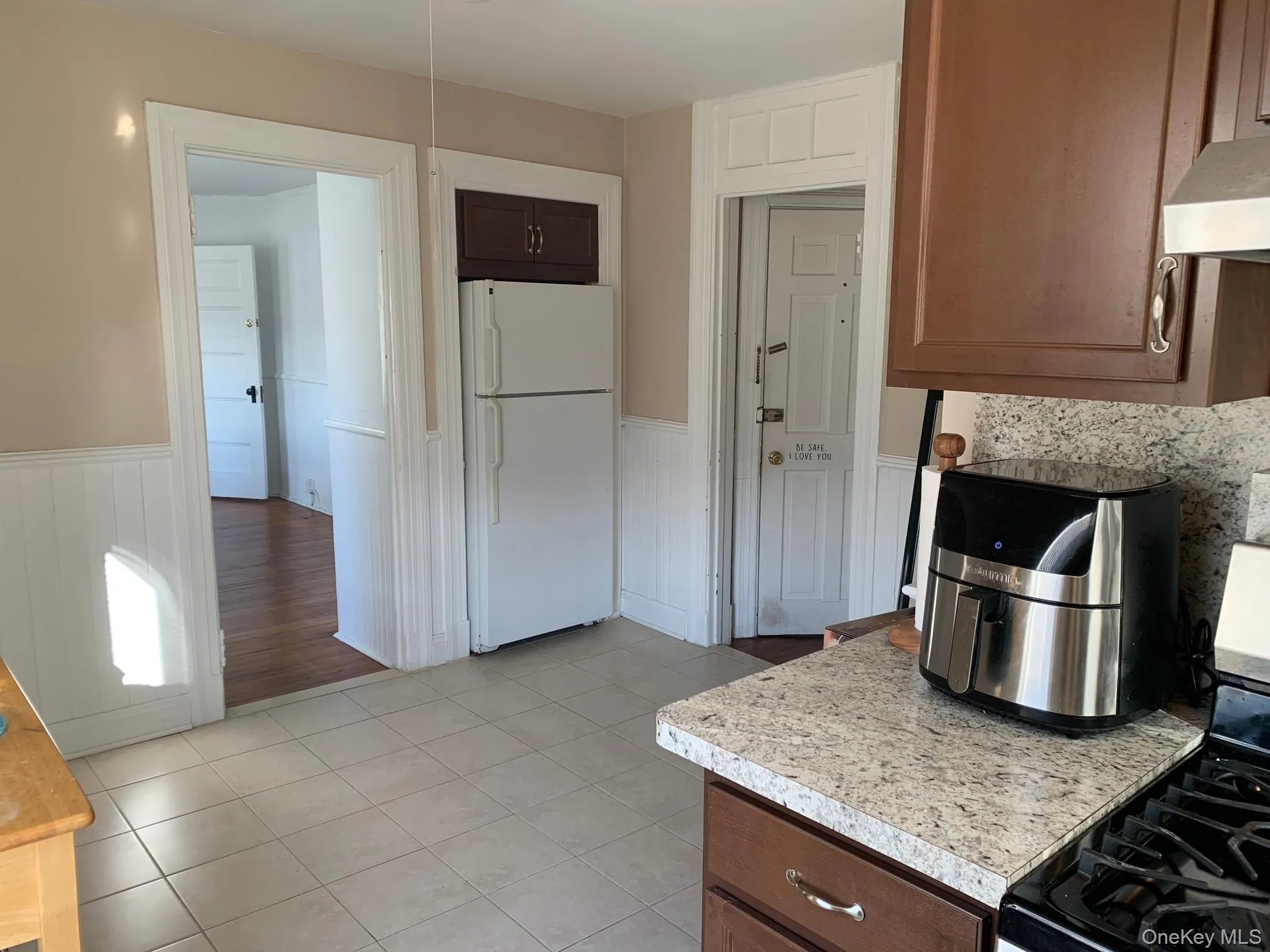 Kitchen featuring gas range, freestanding refrigerator, dark brown cabinetry, light countertops, and a wainscoted wall Kitchen featuring gas range, freestanding refrigerator, dark brown cabinetry, light countertops, and a wainscoted wall