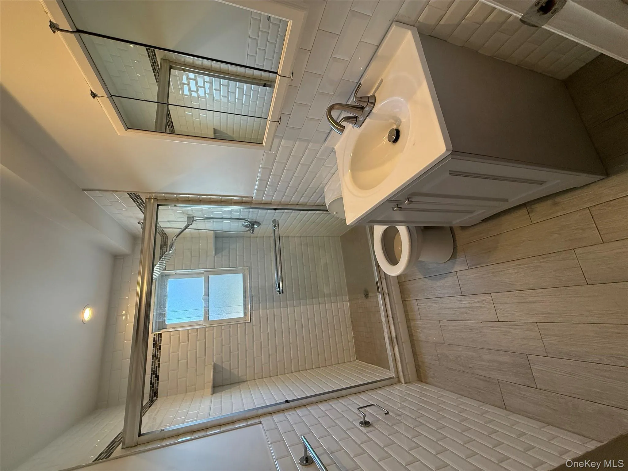 Full bathroom featuring tile walls, wainscoting, vanity, a shower stall, and wood tiled floors Full bathroom featuring tile walls, wainscoting, vanity, a shower stall, and wood tiled floors