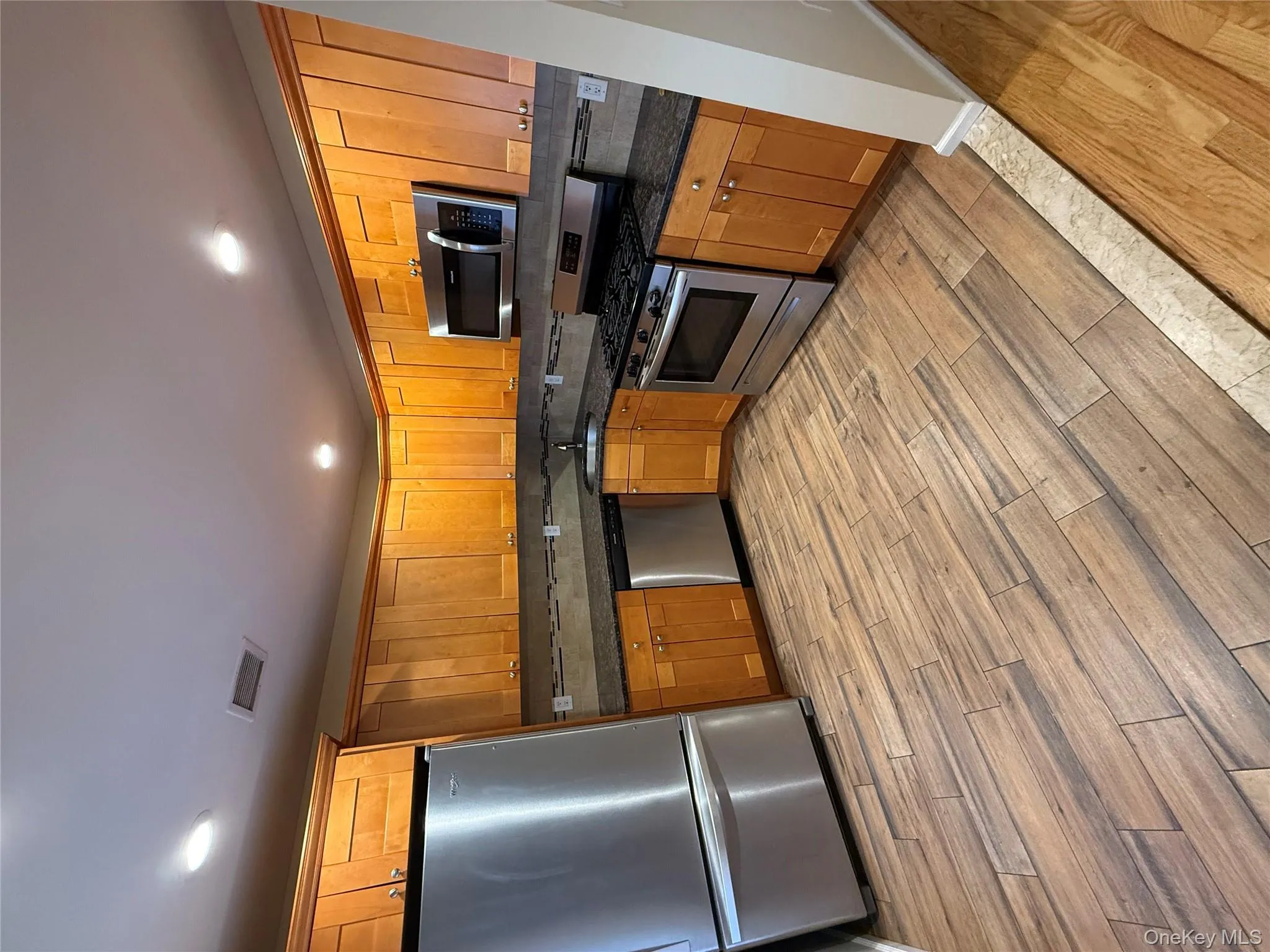 Kitchen featuring stainless steel appliances, brown cabinets, light wood-style flooring, recessed lighting, and dark stone counters Kitchen featuring stainless steel appliances, brown cabinets, light wood-style flooring, recessed lighting, and dark stone counters