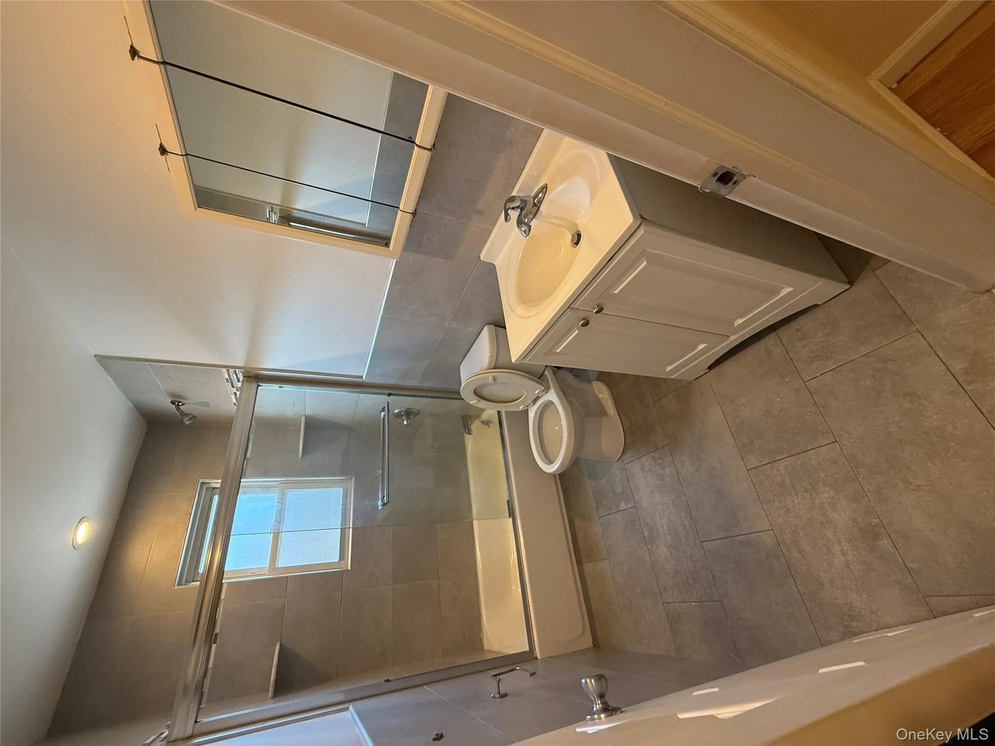 Full bathroom with vanity, tile walls, combined bath / shower with glass door, and a wainscoted wall Full bathroom with vanity, tile walls, combined bath / shower with glass door, and a wainscoted wall