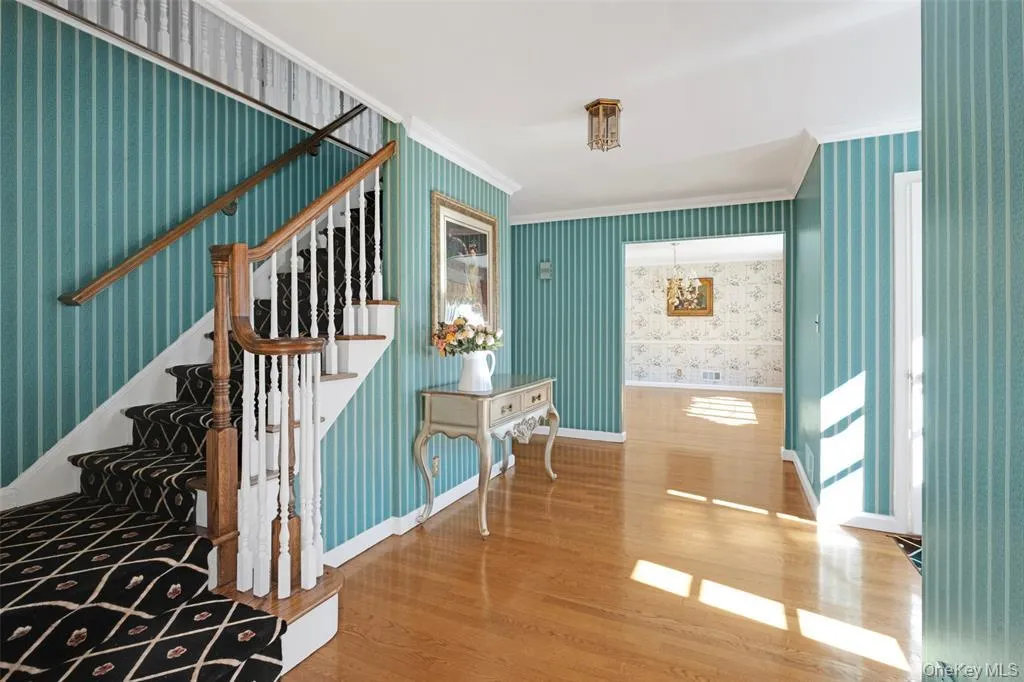 Staircase featuring wood finished floors, wallpapered walls, and crown molding Staircase featuring wood finished floors, wallpapered walls, and crown molding