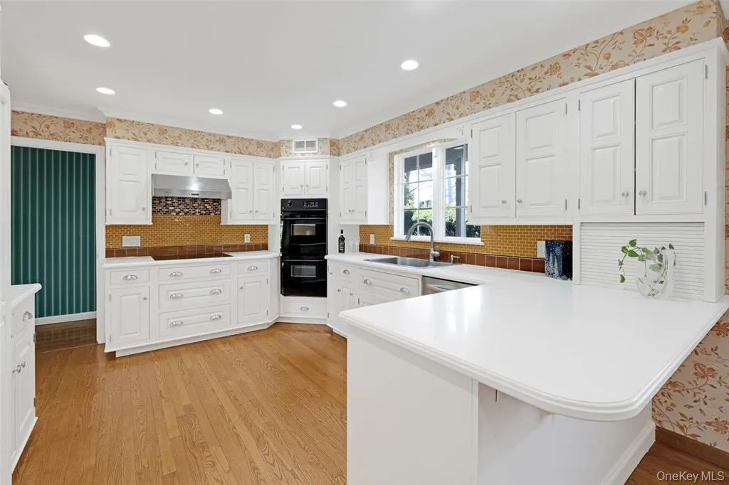 Kitchen with wallpapered walls, a peninsula, white cabinets, light countertops, and light wood-style flooring Kitchen with wallpapered walls, a peninsula, white cabinets, light countertops, and light wood-style flooring