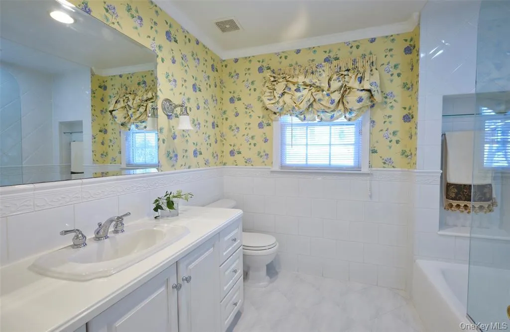 Bathroom featuring a wainscoted wall, tile walls, vanity, and wallpapered walls Bathroom featuring a wainscoted wall, tile walls, vanity, and wallpapered walls