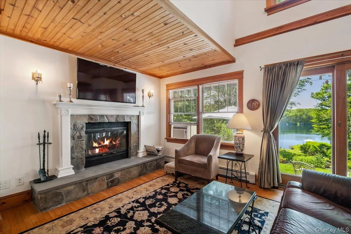 Living area with water views, a glass covered fireplace, wood-type flooring, wood ceiling, and healthy amount of natural light Living area with water views, a glass covered fireplace, wood-type flooring, wood ceiling, and healthy amount of natural light