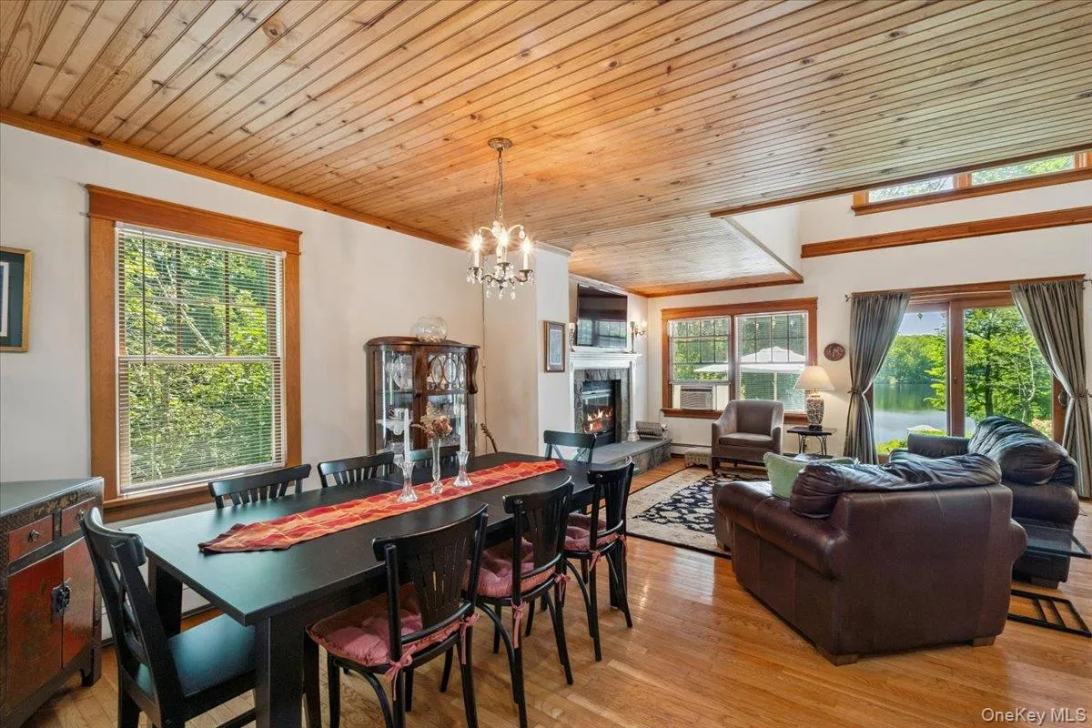 Dining space featuring a warm lit fireplace, wood ceiling, light wood-type flooring, a chandelier, and ornamental molding Dining space featuring a warm lit fireplace, wood ceiling, light wood-type flooring, a chandelier, and ornamental molding