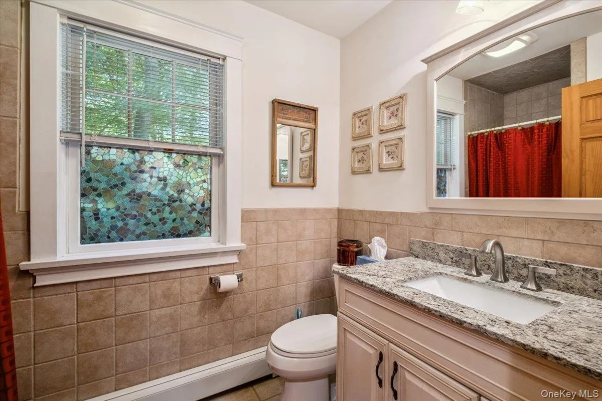 Full bath featuring tile walls, vanity, a baseboard radiator, a wainscoted wall, and curtained shower Full bath featuring tile walls, vanity, a baseboard radiator, a wainscoted wall, and curtained shower