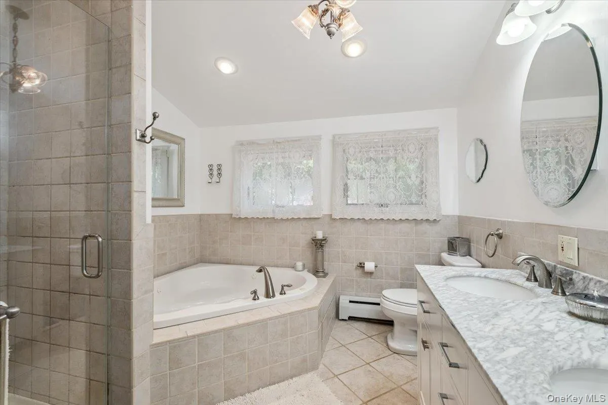 Bathroom with a baseboard heating unit, tile patterned floors, a bath, a stall shower, and double vanity Bathroom with a baseboard heating unit, tile patterned floors, a bath, a stall shower, and double vanity