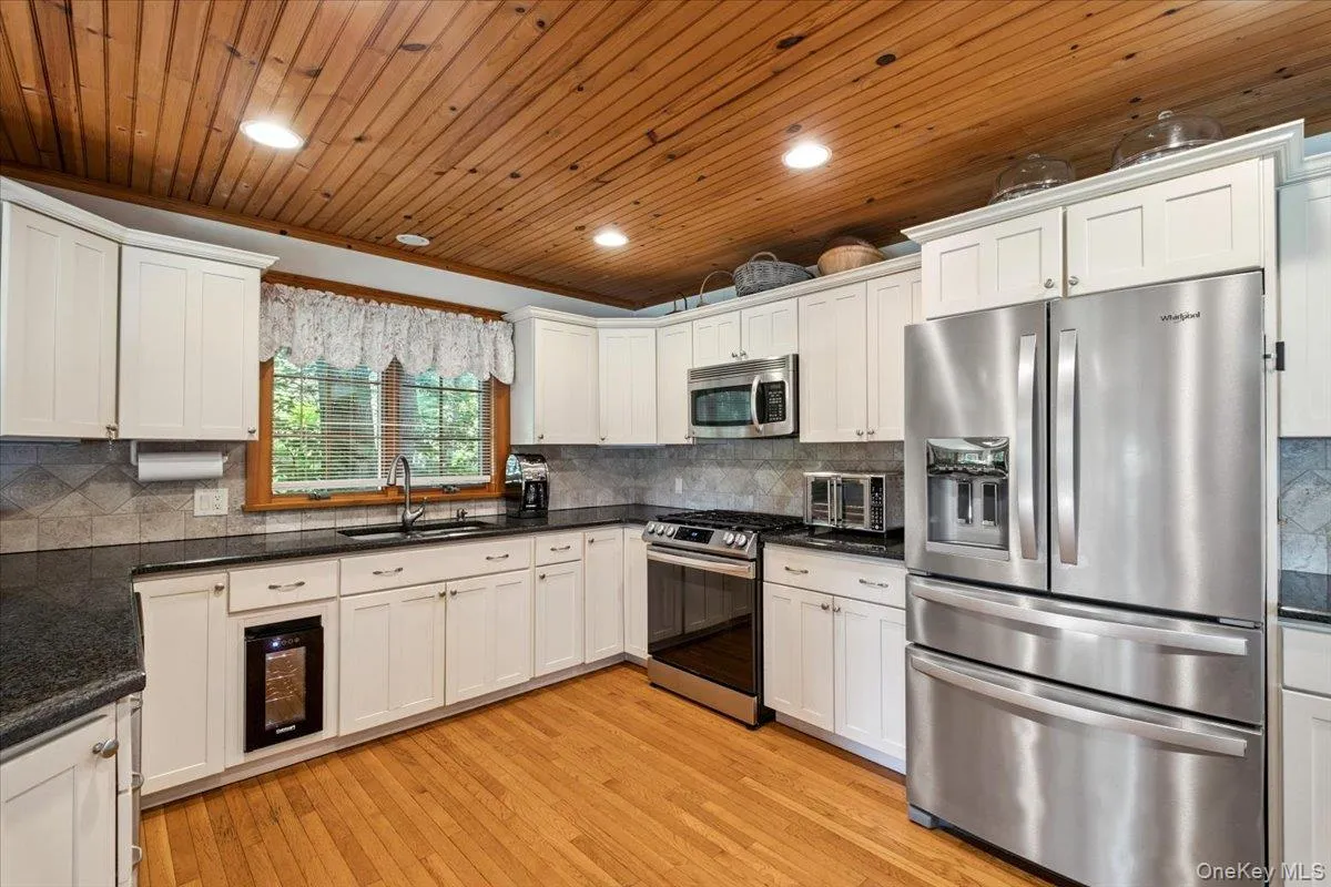 Kitchen featuring stainless steel appliances, wine cooler, wooden ceiling, white cabinetry, and light wood-style flooring Kitchen featuring stainless steel appliances, wine cooler, wooden ceiling, white cabinetry, and light wood-style flooring