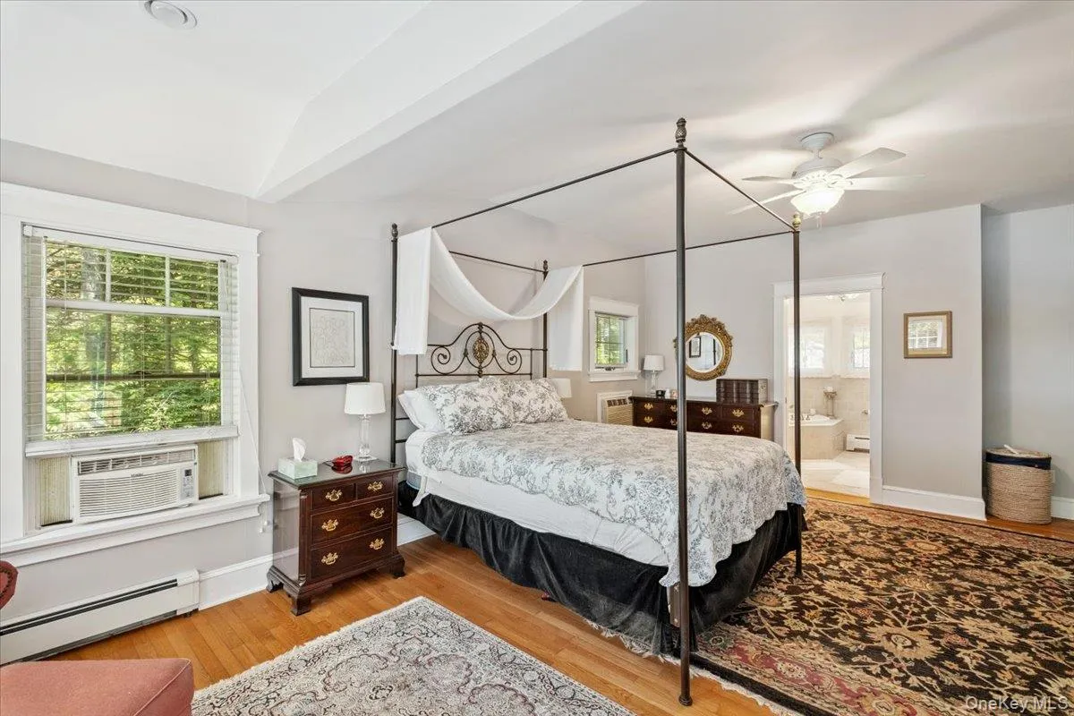 Bedroom with a baseboard heating unit, cooling unit, multiple windows, wood finished floors, and vaulted ceiling Bedroom with a baseboard heating unit, cooling unit, multiple windows, wood finished floors, and vaulted ceiling