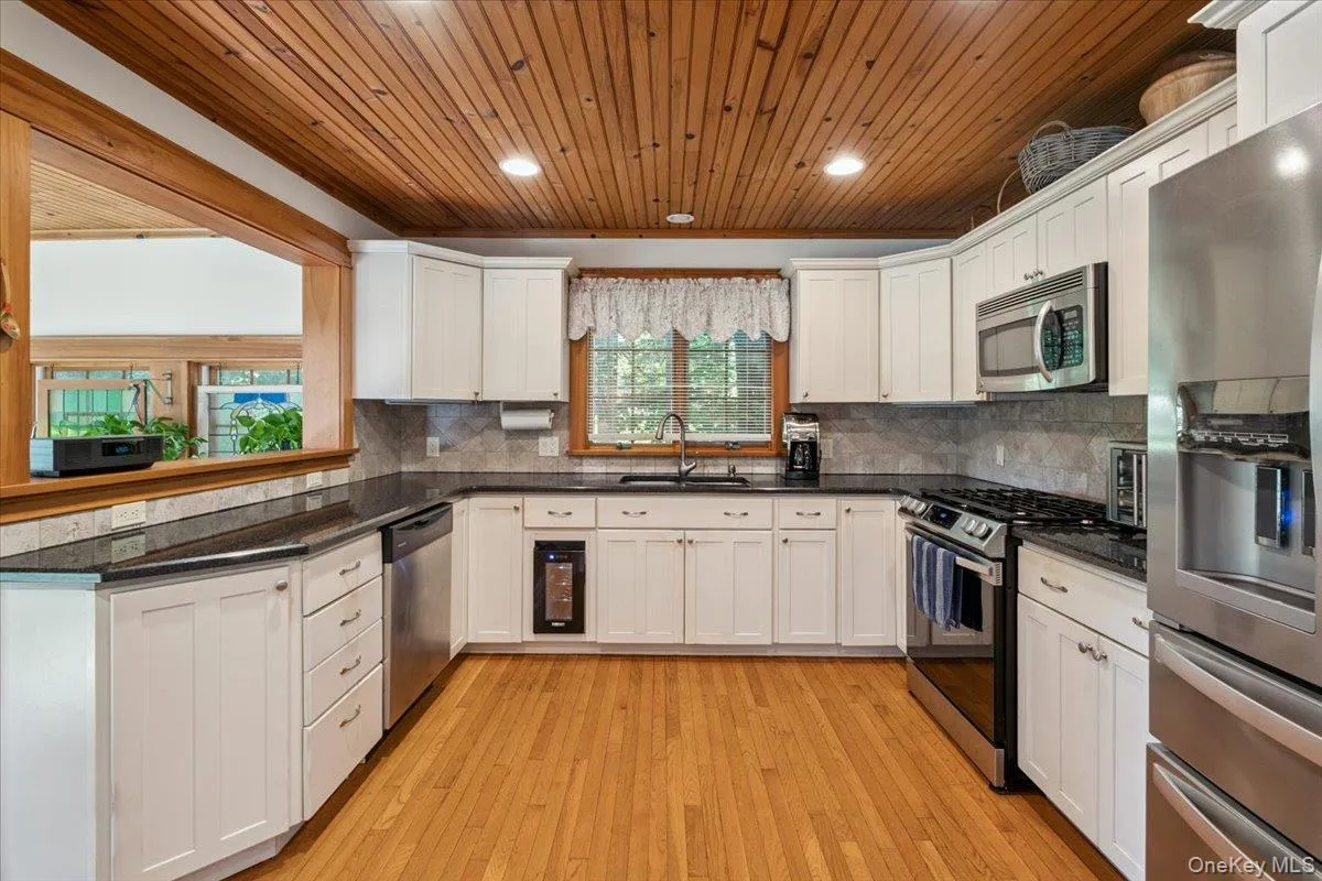 Kitchen with appliances with stainless steel finishes, wood ceiling, white cabinetry, light wood-style flooring, and backsplash Kitchen with appliances with stainless steel finishes, wood ceiling, white cabinetry, light wood-style flooring, and backsplash