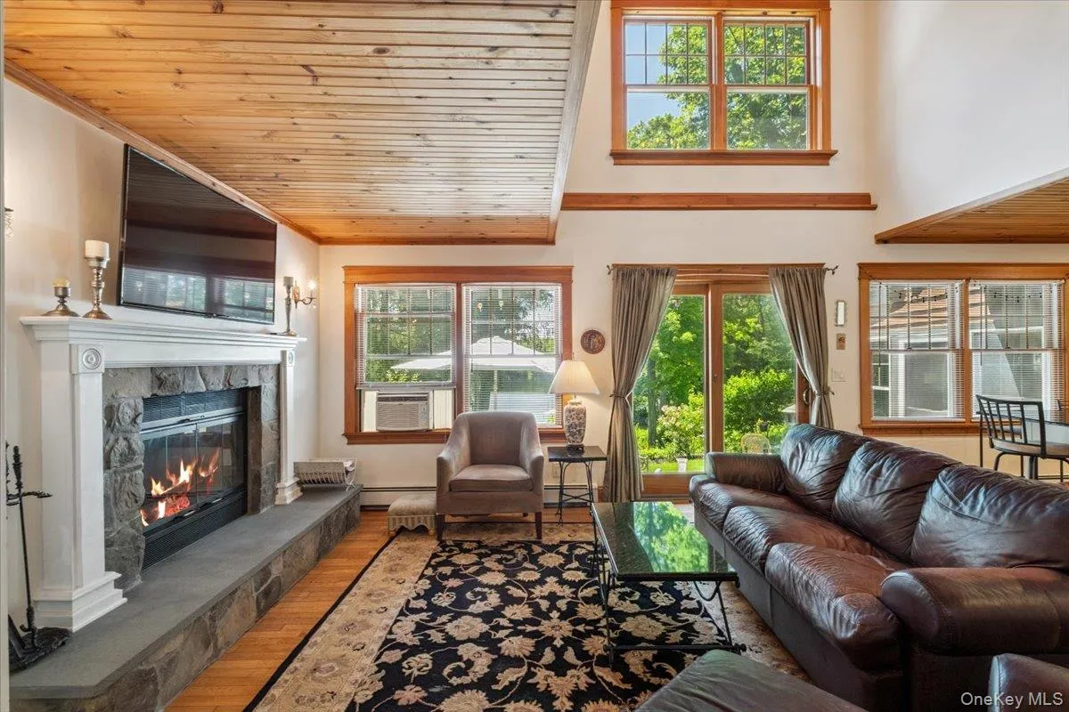 Living area with a glass covered fireplace, wood ceiling, cooling unit, wood finished floors, and a baseboard heating unit Living area with a glass covered fireplace, wood ceiling, cooling unit, wood finished floors, and a baseboard heating unit