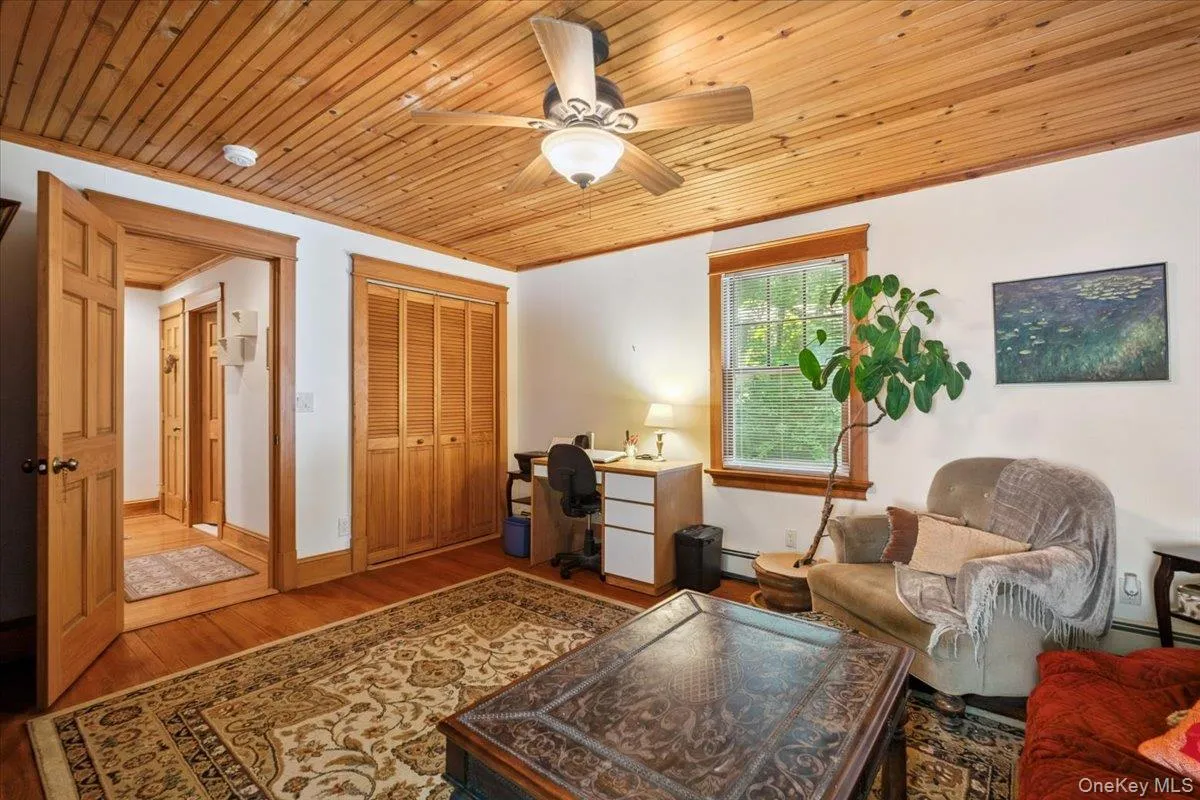 Living room with an office area, wood finished floors, wood ceiling, a ceiling fan, and a baseboard heating unit Living room with an office area, wood finished floors, wood ceiling, a ceiling fan, and a baseboard heating unit