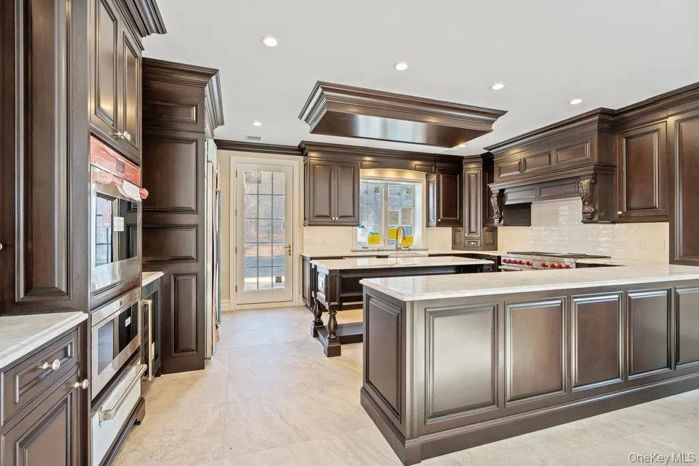 Kitchen with dark brown cabinets, a peninsula, tasteful backsplash, crown molding, and recessed lighting Kitchen with dark brown cabinets, a peninsula, tasteful backsplash, crown molding, and recessed lighting