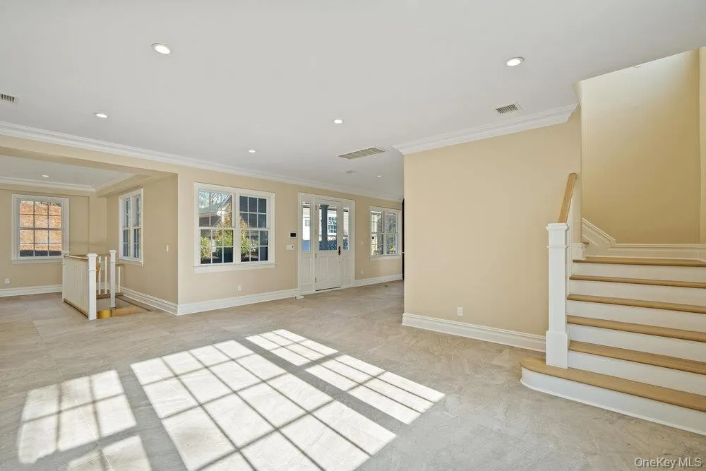 Unfurnished living room featuring stairway, recessed lighting, plenty of natural light, and ornamental molding Unfurnished living room featuring stairway, recessed lighting, plenty of natural light, and ornamental molding