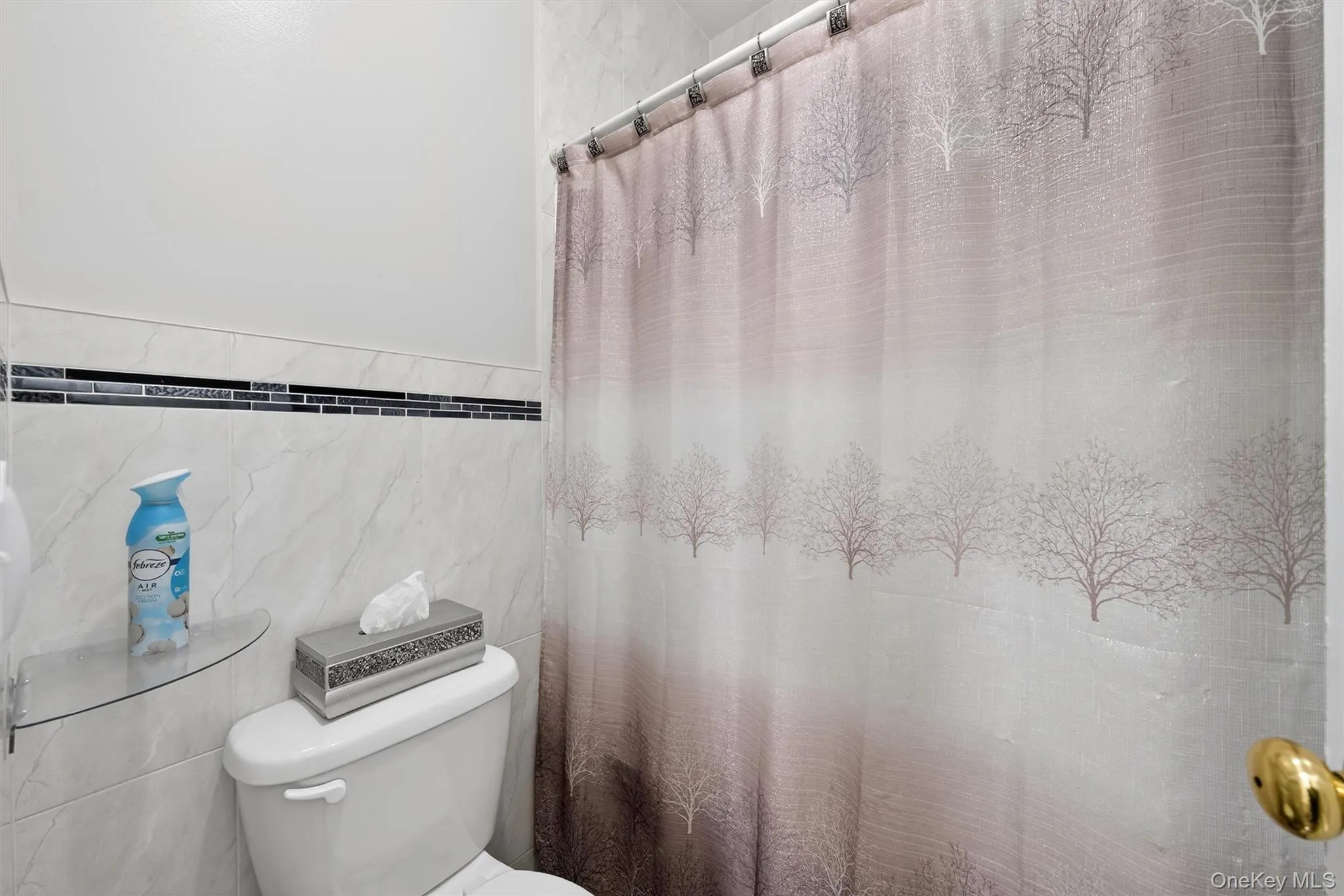 Full bath with tile walls, a shower with curtain, and wainscoting Full bath with tile walls, a shower with curtain, and wainscoting