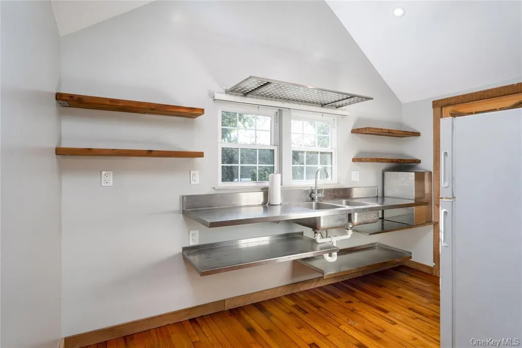 Kitchen with open shelves, stainless steel counters, freestanding refrigerator, vaulted ceiling, and light wood-style flooring Kitchen with open shelves, stainless steel counters, freestanding refrigerator, vaulted ceiling, and light wood-style flooring