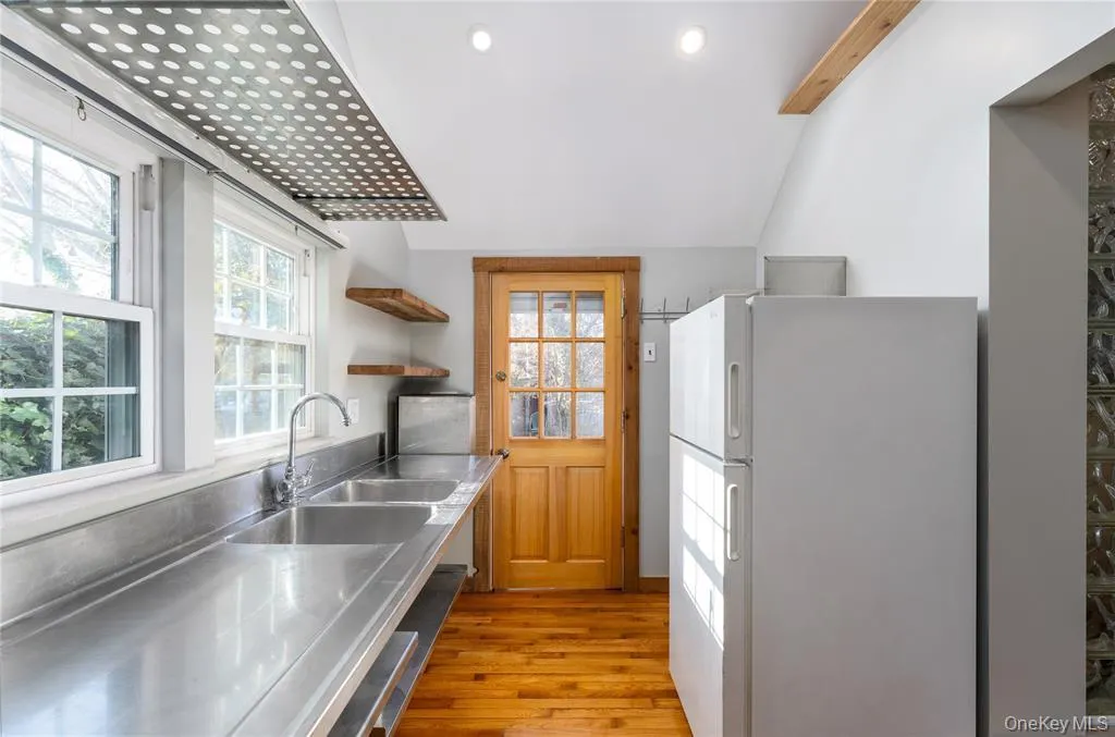 Kitchen featuring stainless steel countertops, freestanding refrigerator, healthy amount of natural light, open shelves, and vaulted ceiling Kitchen featuring stainless steel countertops, freestanding refrigerator, healthy amount of natural light, open shelves, and vaulted ceiling
