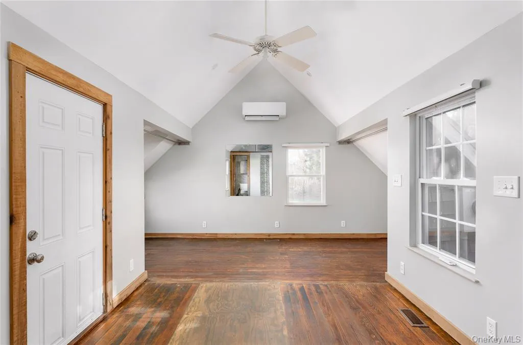 Additional living space with lofted ceiling, dark wood finished floors, ceiling fan, and a wall mounted air conditioner Additional living space with lofted ceiling, dark wood finished floors, ceiling fan, and a wall mounted air conditioner