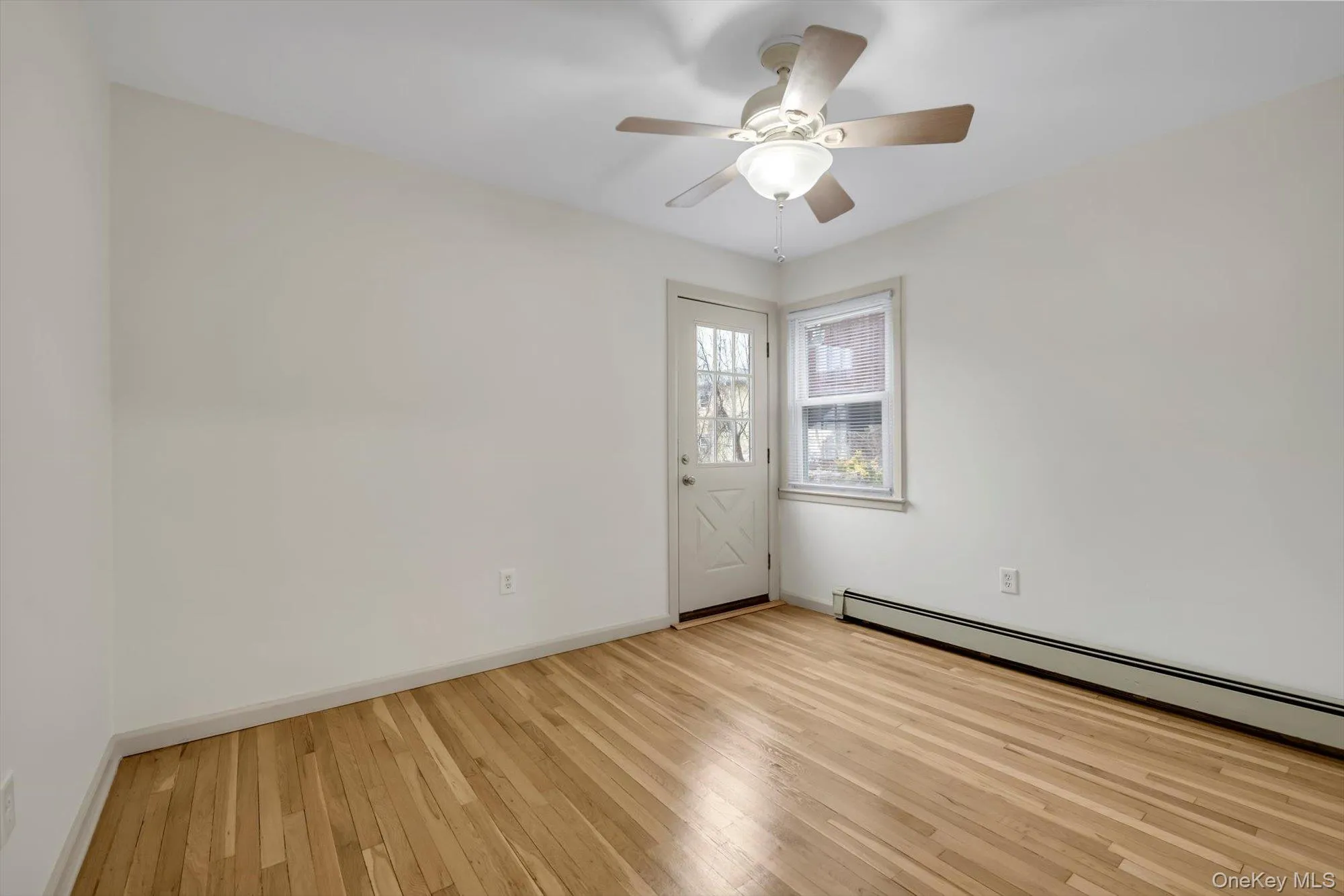 Unfurnished room featuring baseboard heating, light wood finished floors, and a ceiling fan Unfurnished room featuring baseboard heating, light wood finished floors, and a ceiling fan