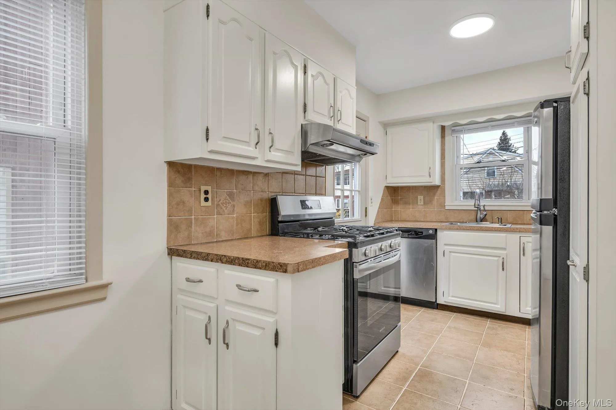 Kitchen featuring appliances with stainless steel finishes, white cabinetry, under cabinet range hood, light tile patterned floors, and tasteful backsplash Kitchen featuring appliances with stainless steel finishes, white cabinetry, under cabinet range hood, light tile patterned floors, and tasteful backsplash
