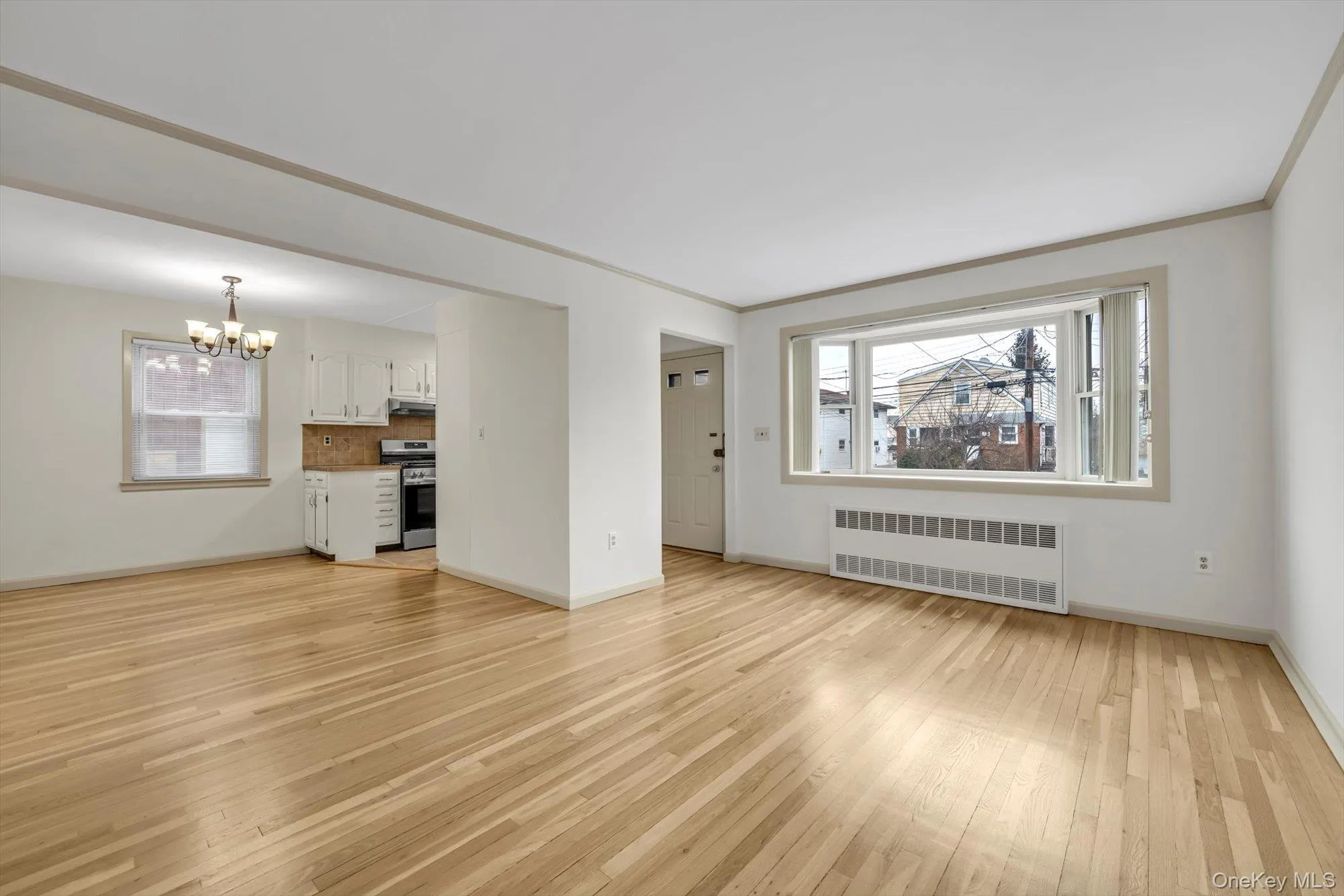 Unfurnished living room with radiator heating unit, light wood-type flooring, a chandelier, and crown molding Unfurnished living room with radiator heating unit, light wood-type flooring, a chandelier, and crown molding