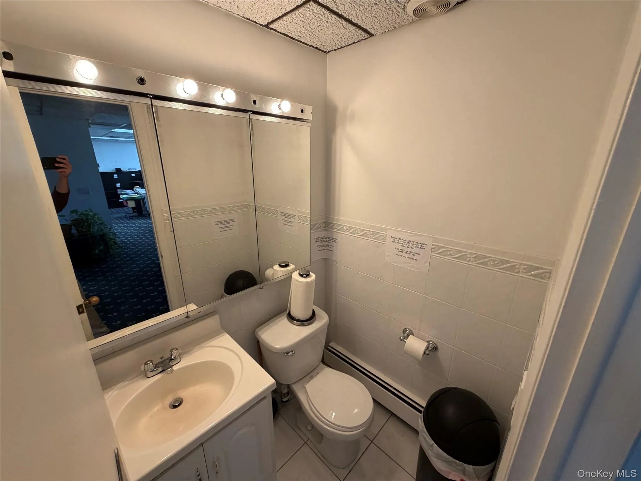 Half bathroom featuring baseboard heating, vanity, light tile patterned flooring, tile walls, and a wainscoted wall Half bathroom featuring baseboard heating, vanity, light tile patterned flooring, tile walls, and a wainscoted wall
