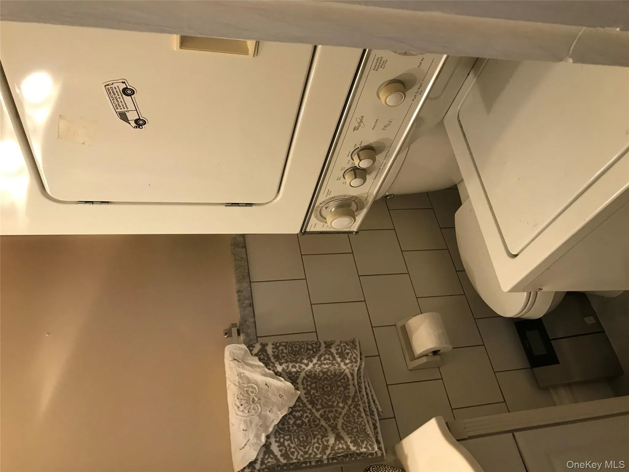 Washroom with tile walls, stacked washing machine and dryer, and a wainscoted wall Washroom with tile walls, stacked washing machine and dryer, and a wainscoted wall