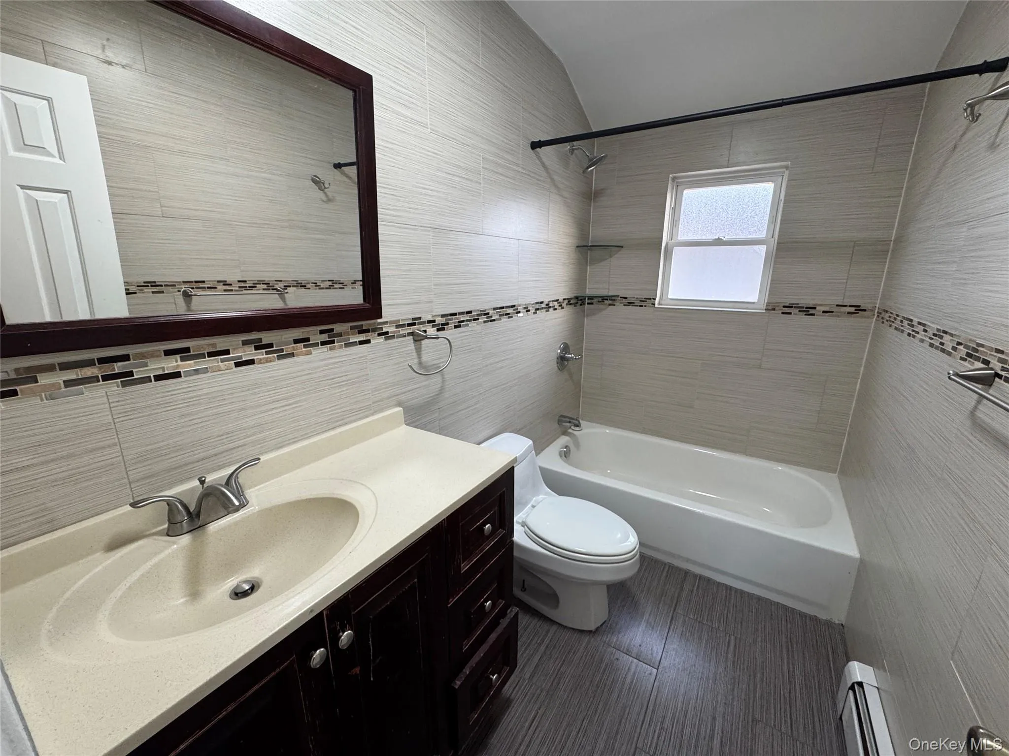 Full bathroom featuring washtub / shower combination, vanity, tile walls, a baseboard heating unit, and vaulted ceiling Full bathroom featuring washtub / shower combination, vanity, tile walls, a baseboard heating unit, and vaulted ceiling
