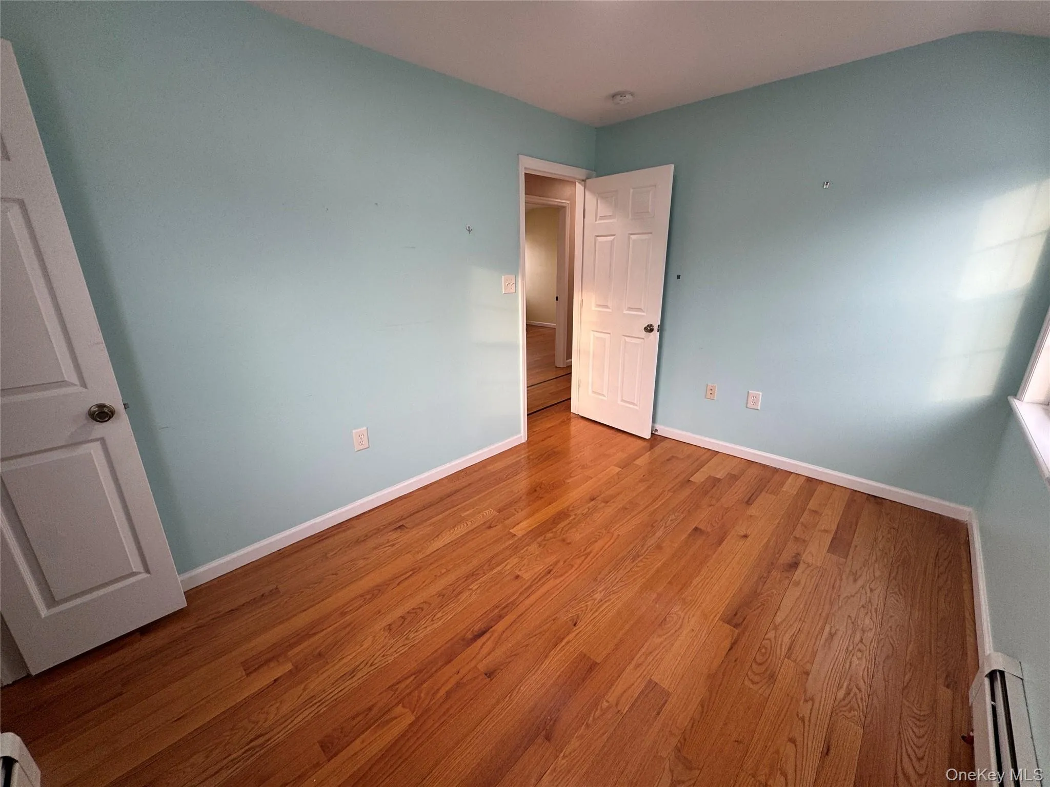 Unfurnished bedroom featuring baseboard heating and wood finished floors Unfurnished bedroom featuring baseboard heating and wood finished floors