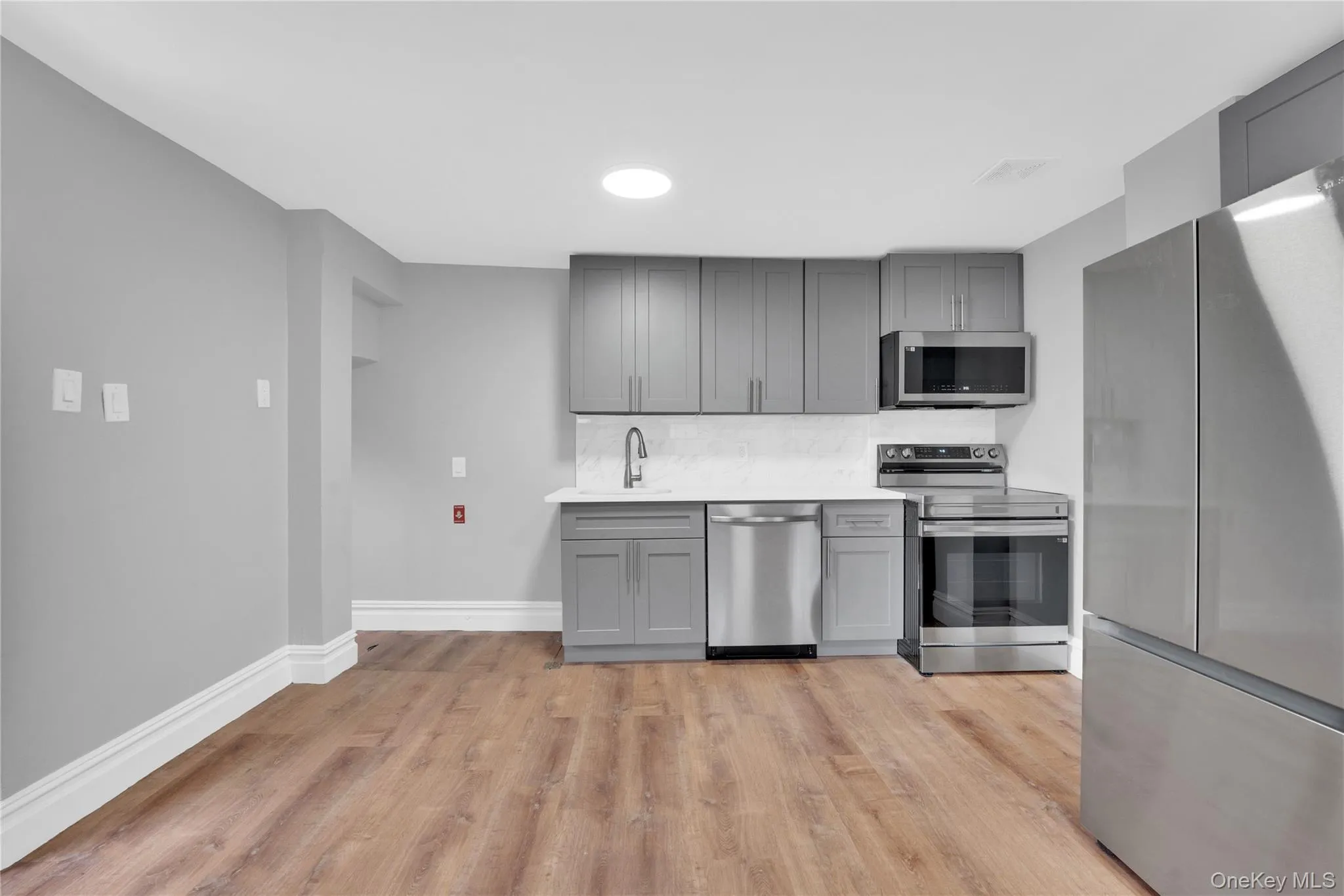 Kitchen featuring appliances with stainless steel finishes, gray cabinetry, decorative backsplash, light wood-type flooring, and light stone countertops Kitchen featuring appliances with stainless steel finishes, gray cabinetry, decorative backsplash, light wood-type flooring, and light stone countertops