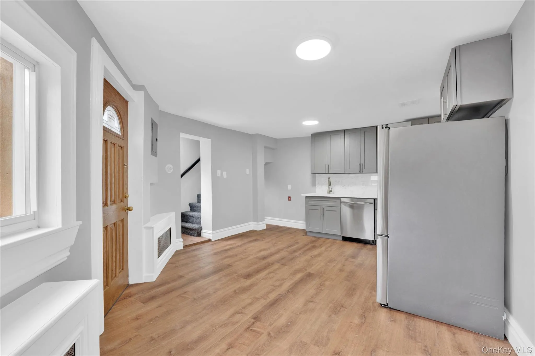 Kitchen with gray cabinets, appliances with stainless steel finishes, light countertops, light wood-type flooring, and backsplash Kitchen with gray cabinets, appliances with stainless steel finishes, light countertops, light wood-type flooring, and backsplash