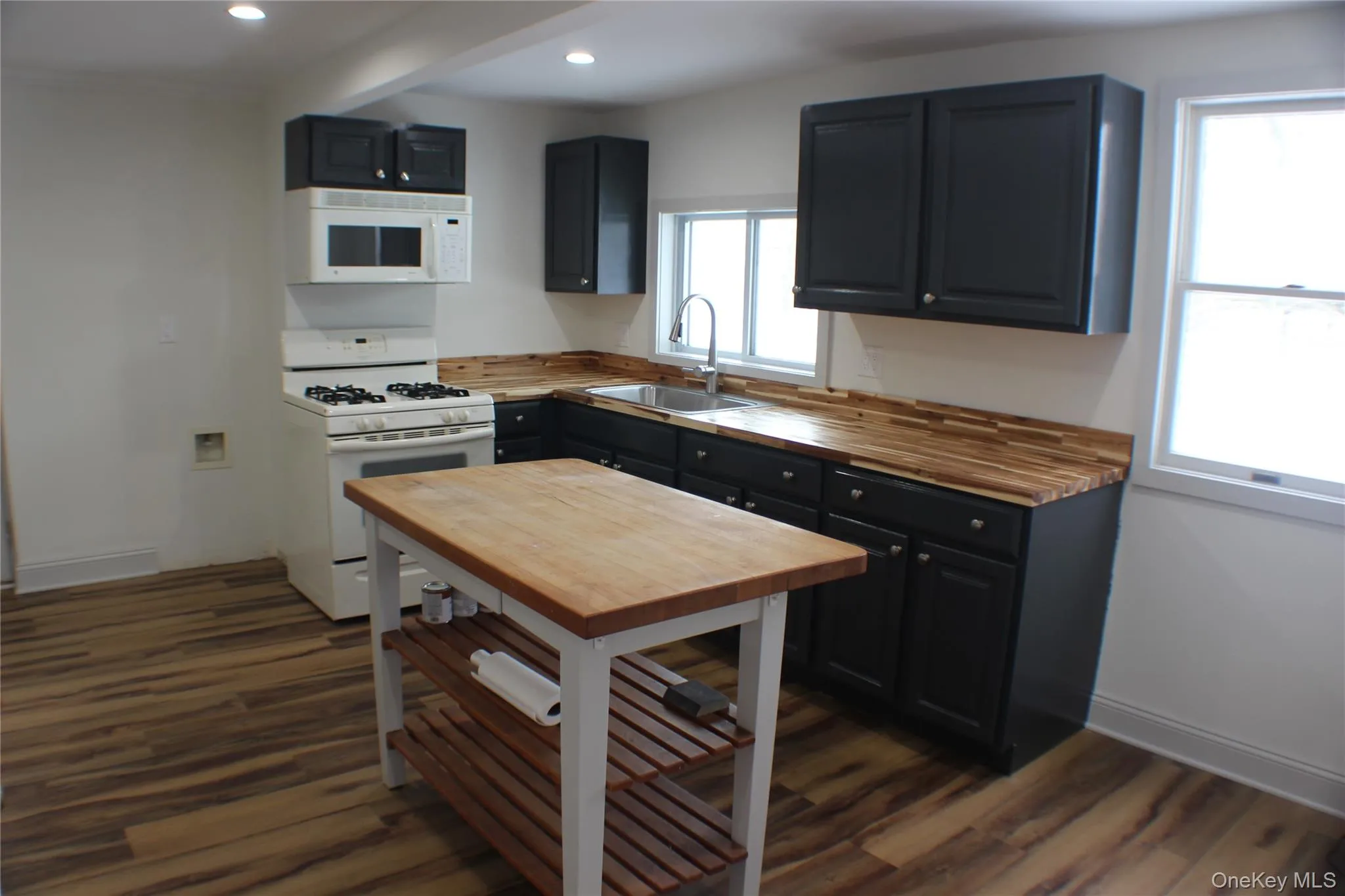 Kitchen with white appliances, wooden counters, recessed lighting, dark wood finished floors, and dark cabinetry Kitchen with white appliances, wooden counters, recessed lighting, dark wood finished floors, and dark cabinetry