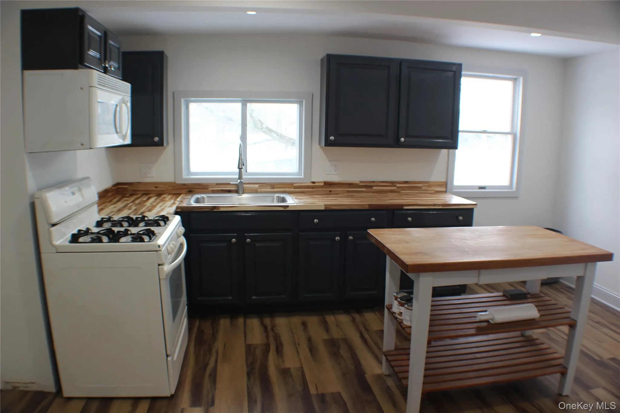Kitchen with white appliances, butcher block counters, dark wood finished floors, recessed lighting, and plenty of natural light Kitchen with white appliances, butcher block counters, dark wood finished floors, recessed lighting, and plenty of natural light