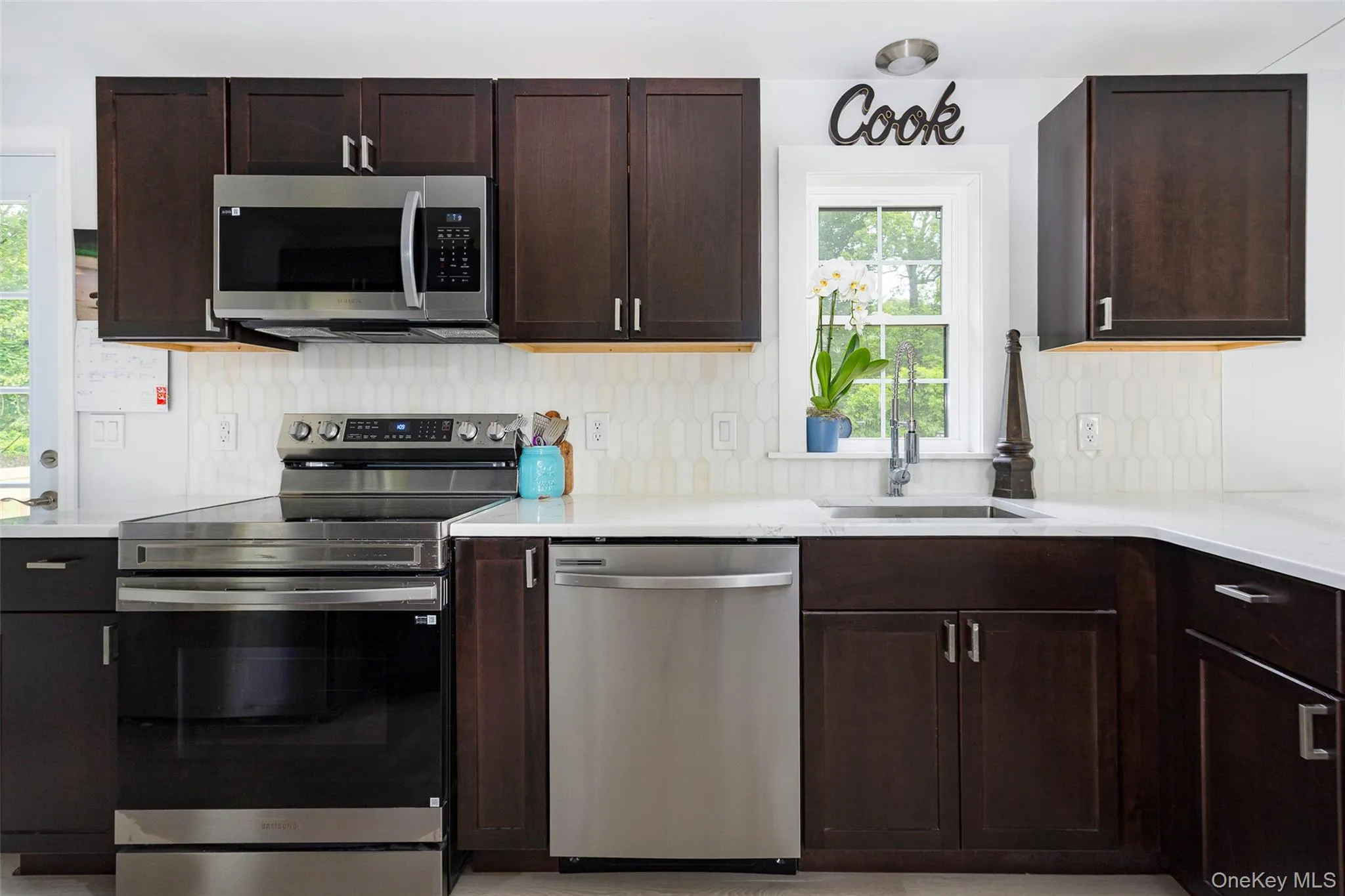 Kitchen with stainless steel appliances, dark brown cabinetry, light countertops, and decorative backsplash Kitchen with stainless steel appliances, dark brown cabinetry, light countertops, and decorative backsplash