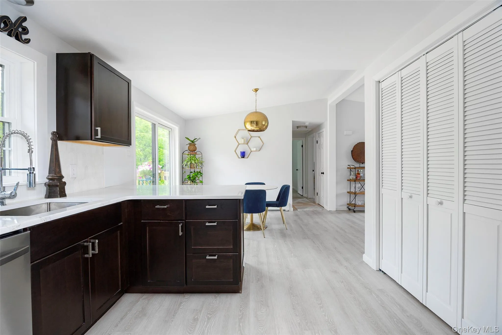 Kitchen with stainless steel dishwasher, light wood-style flooring, dark brown cabinetry, lofted ceiling, and light countertops Kitchen with stainless steel dishwasher, light wood-style flooring, dark brown cabinetry, lofted ceiling, and light countertops