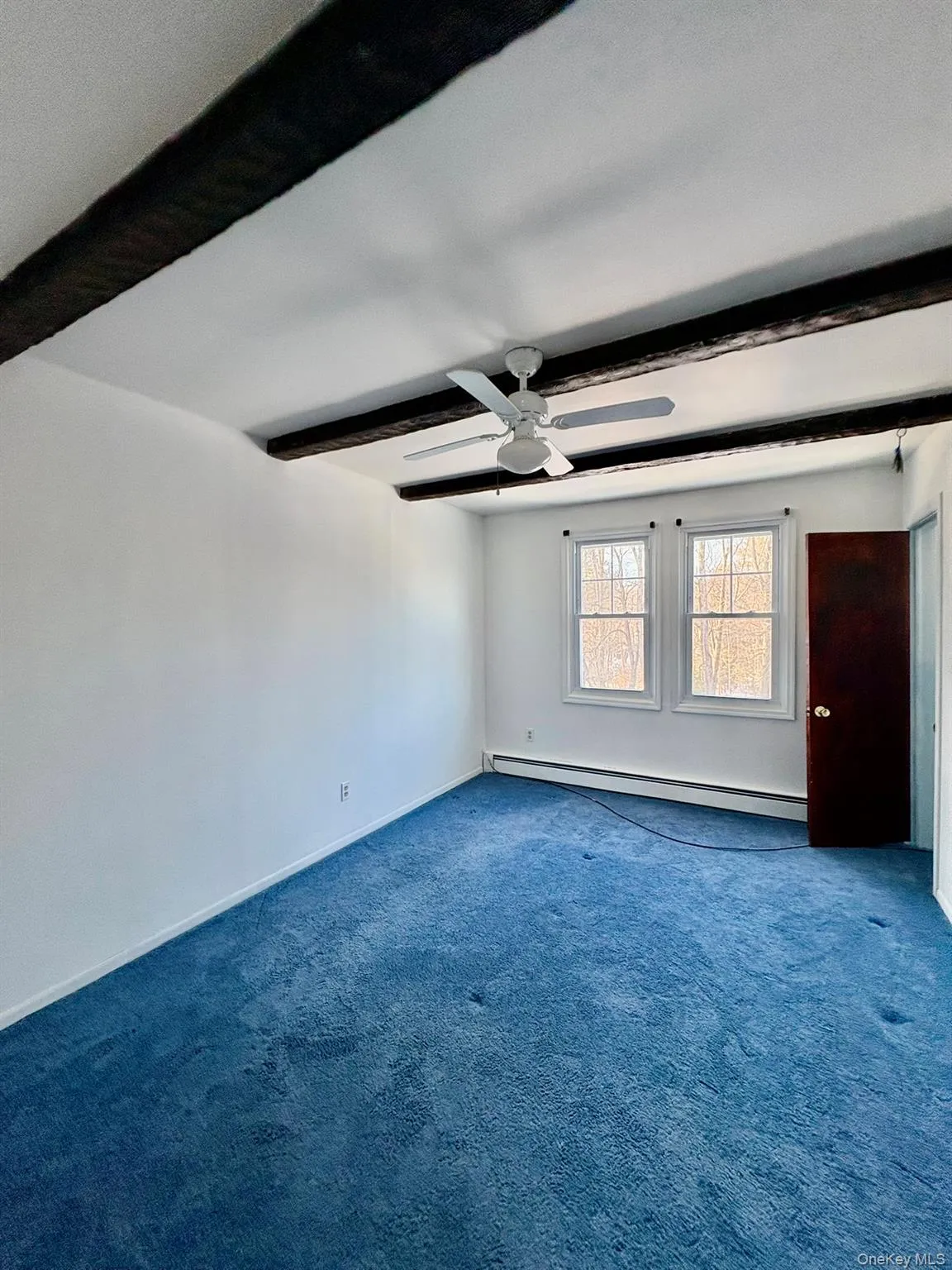 Carpeted spare room with beam ceiling, a baseboard heating unit, and a ceiling fan Carpeted spare room with beam ceiling, a baseboard heating unit, and a ceiling fan